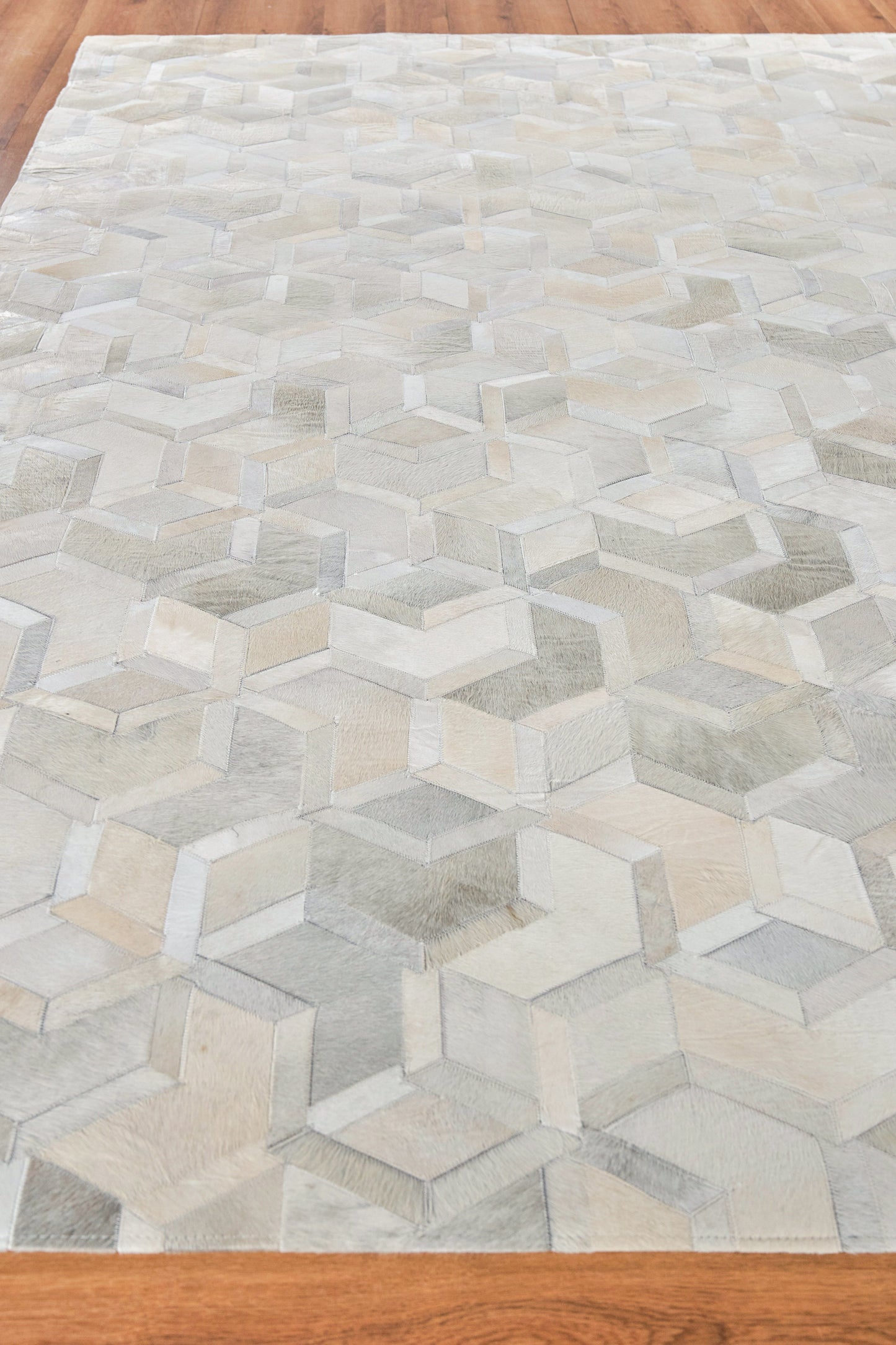 Neutral-toned rug with a 3D cube illusion pattern in ivory, beige & gray on wood floor.