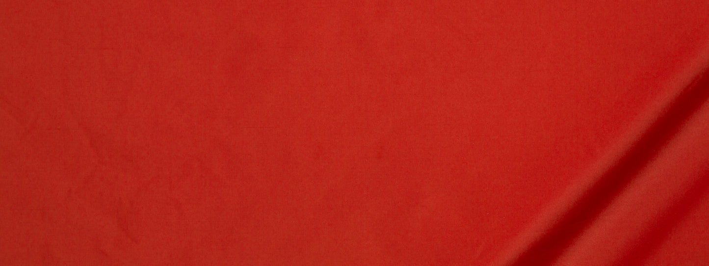 Bright red fabric close-up with a diagonal seam and smooth matte texture.