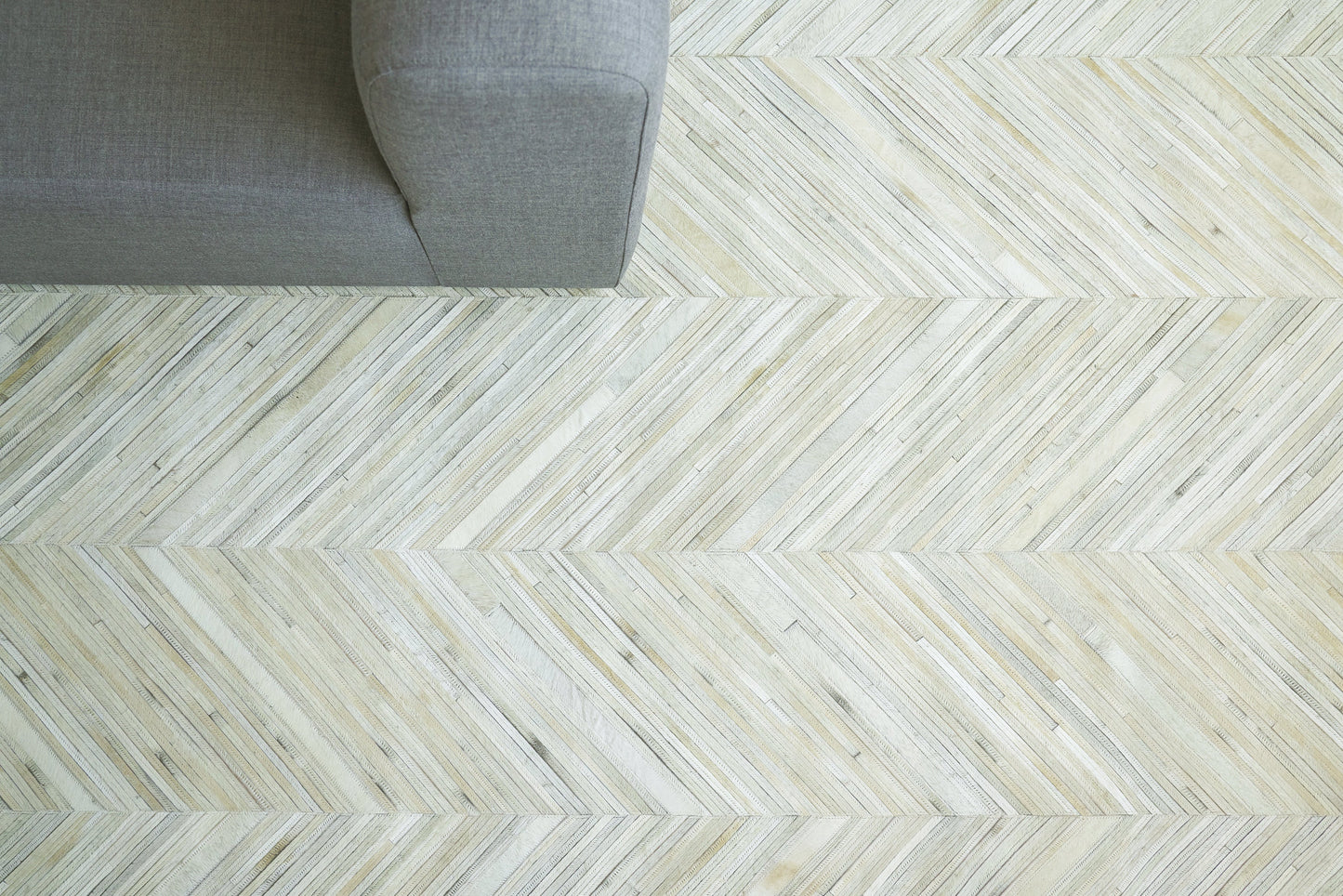 Grey hide rug with hand-stitched detail on light whitewashed chevron wood flooring with diagonal planks.