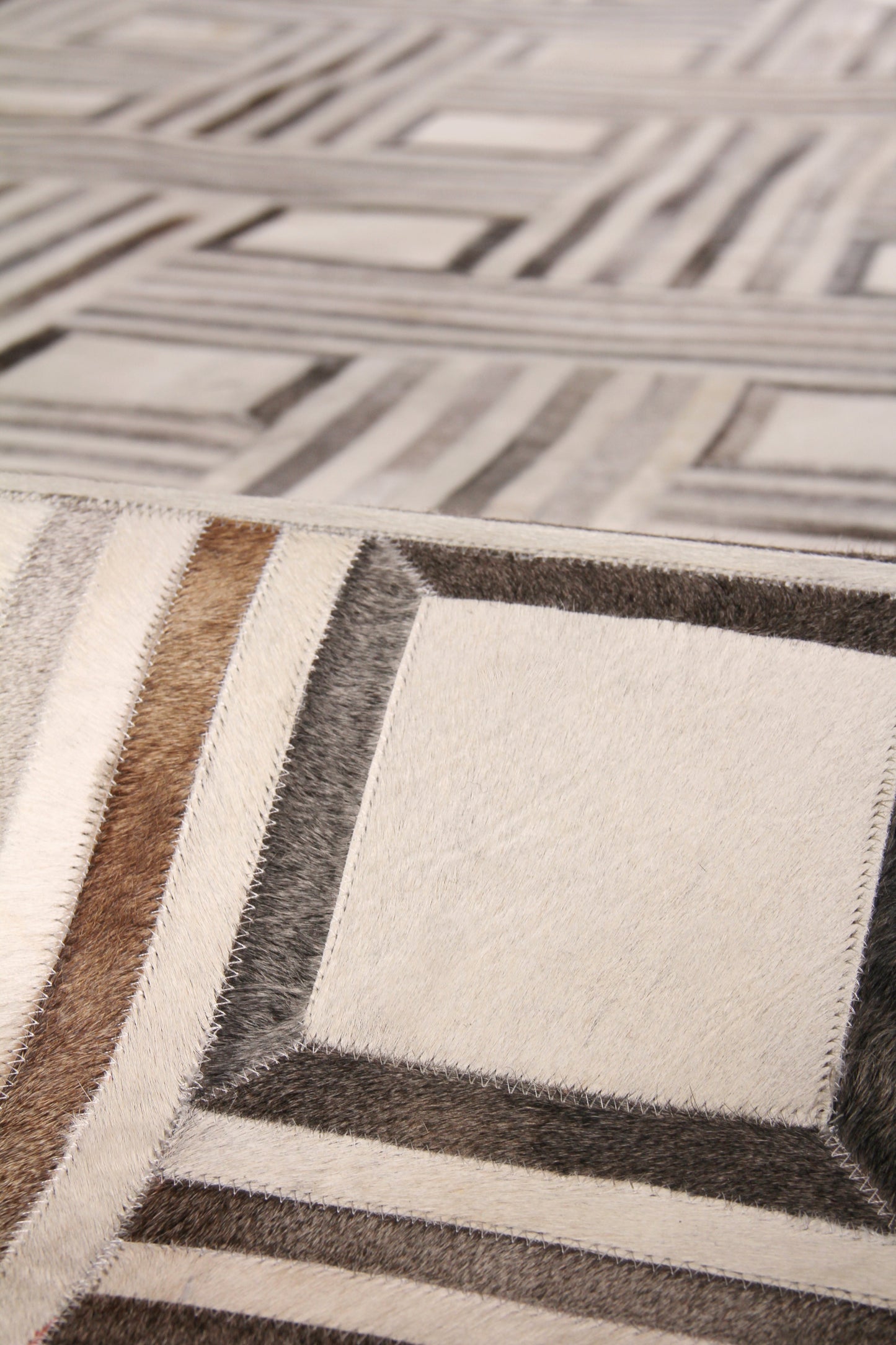 Natural hide rug in cream and taupe tones; indoor, hand-stitched.