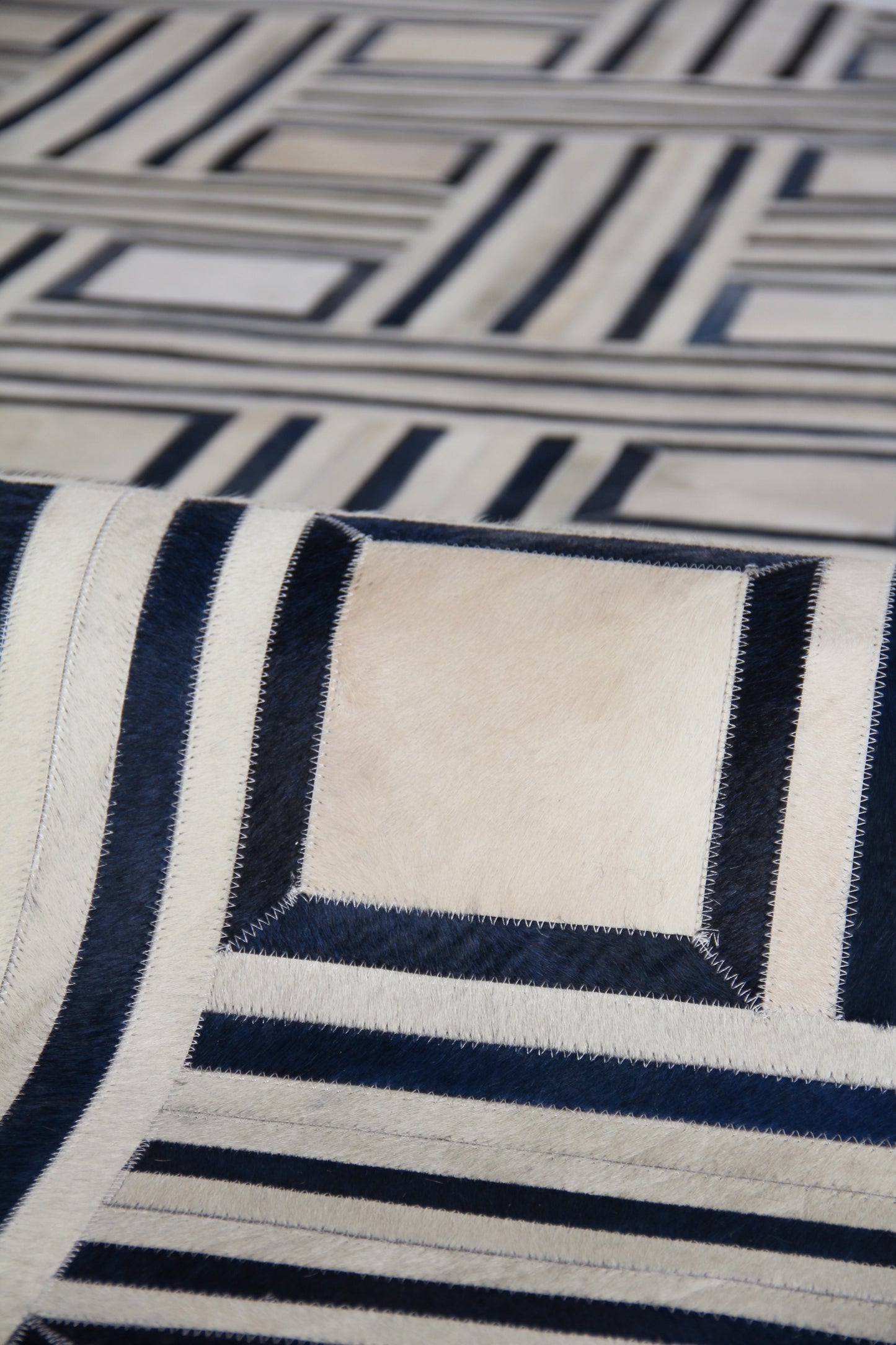 Natural hide indoor hand-stitched rug in navy blue and ivory with geometric framed square motifs; 5' x 8'.