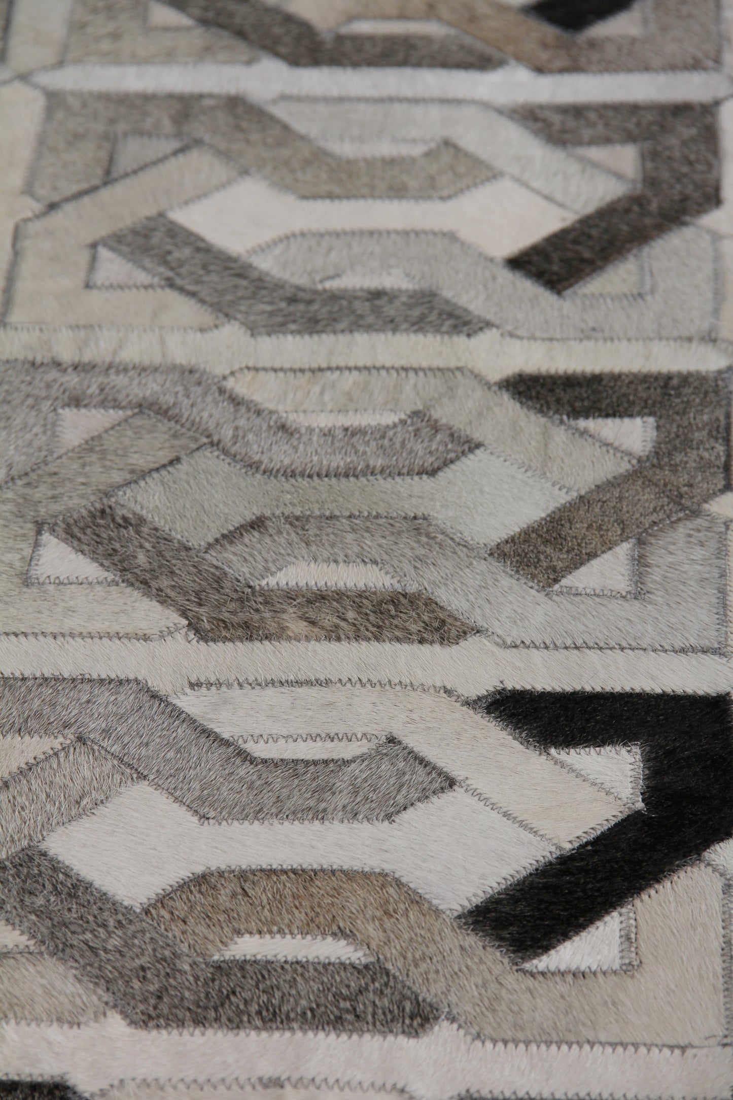 Natural hide indoor hand-stitched rug with a textured surface and repeating interlocking hexagon pattern in gray, beige and black.