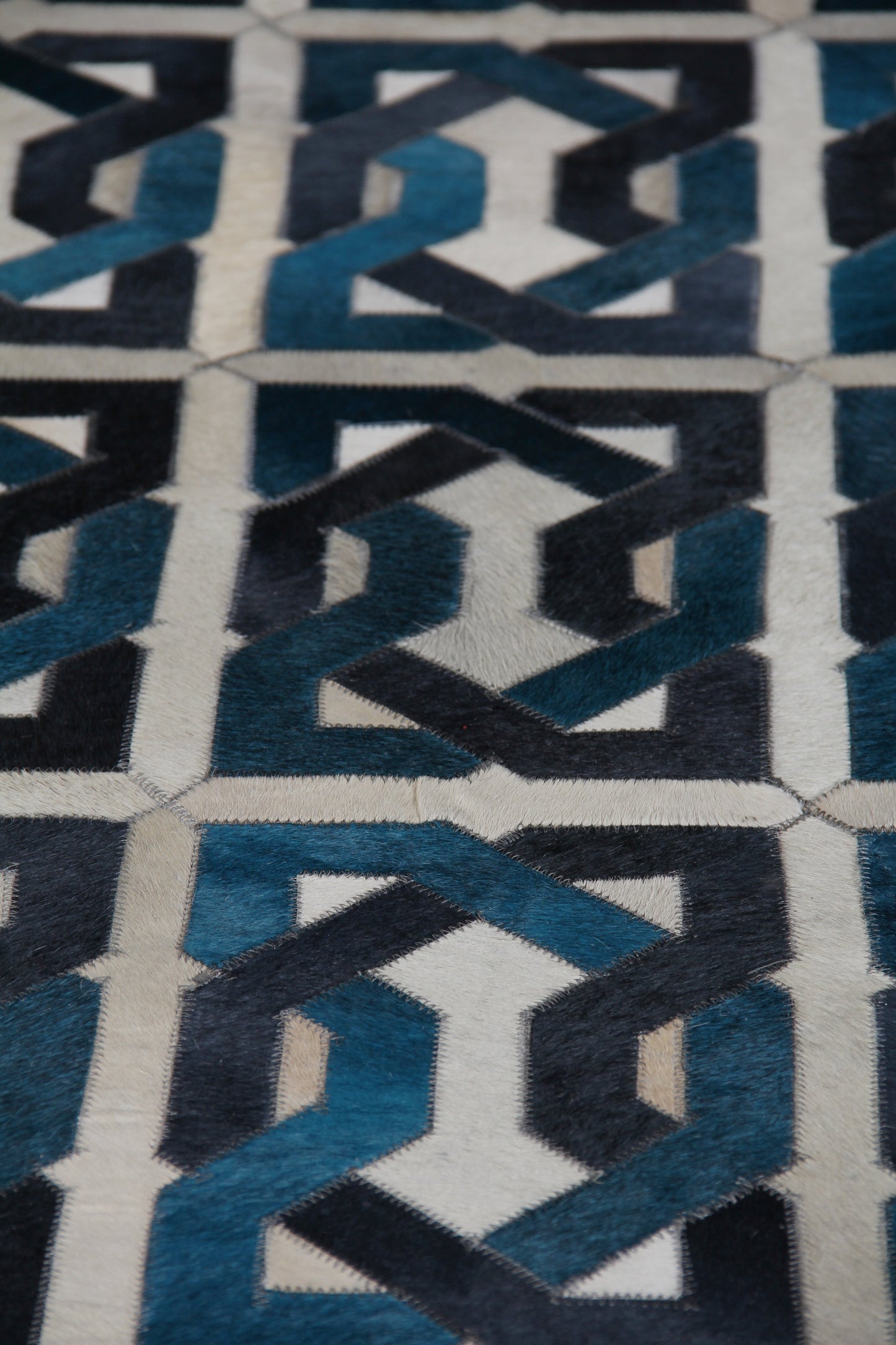 Close-up of blue interlocking hexagon pattern on a natural hide rug in navy & teal with white stitching (5' x 8').
