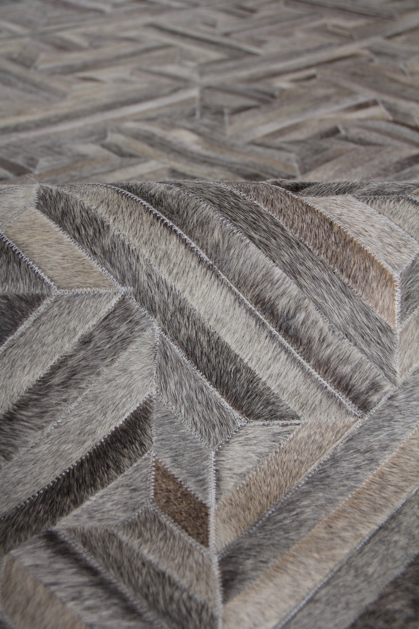 Natural hide indoor hand-stitched rug with a geometric pattern in grey, taupe and beige.