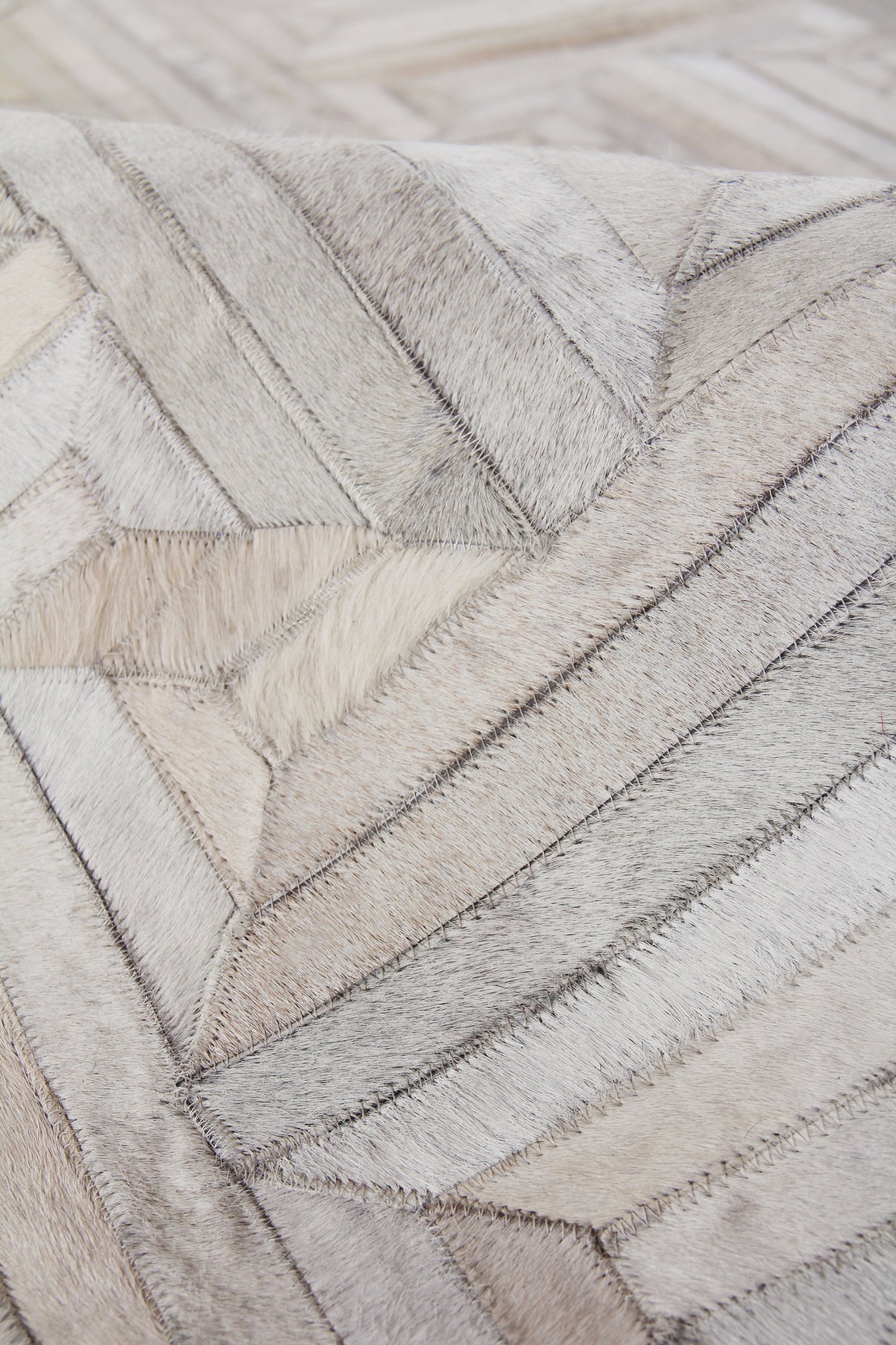 Natural hide rug with chevron patchwork in grey and beige tones; indoor, hand-stitched details.