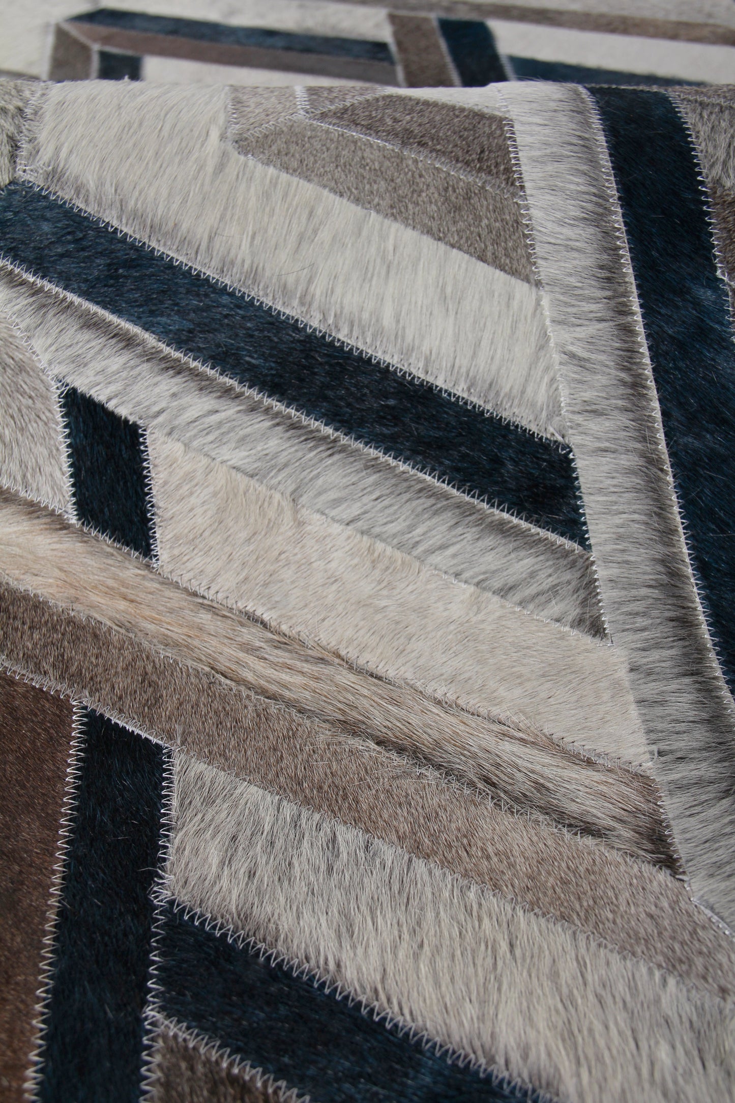 Natural hide indoor hand-stitched rug with geometric pattern; diagonal chevron panels in cream, beige, brown and navy; zigzag stitched seams; size 5' x 8'.