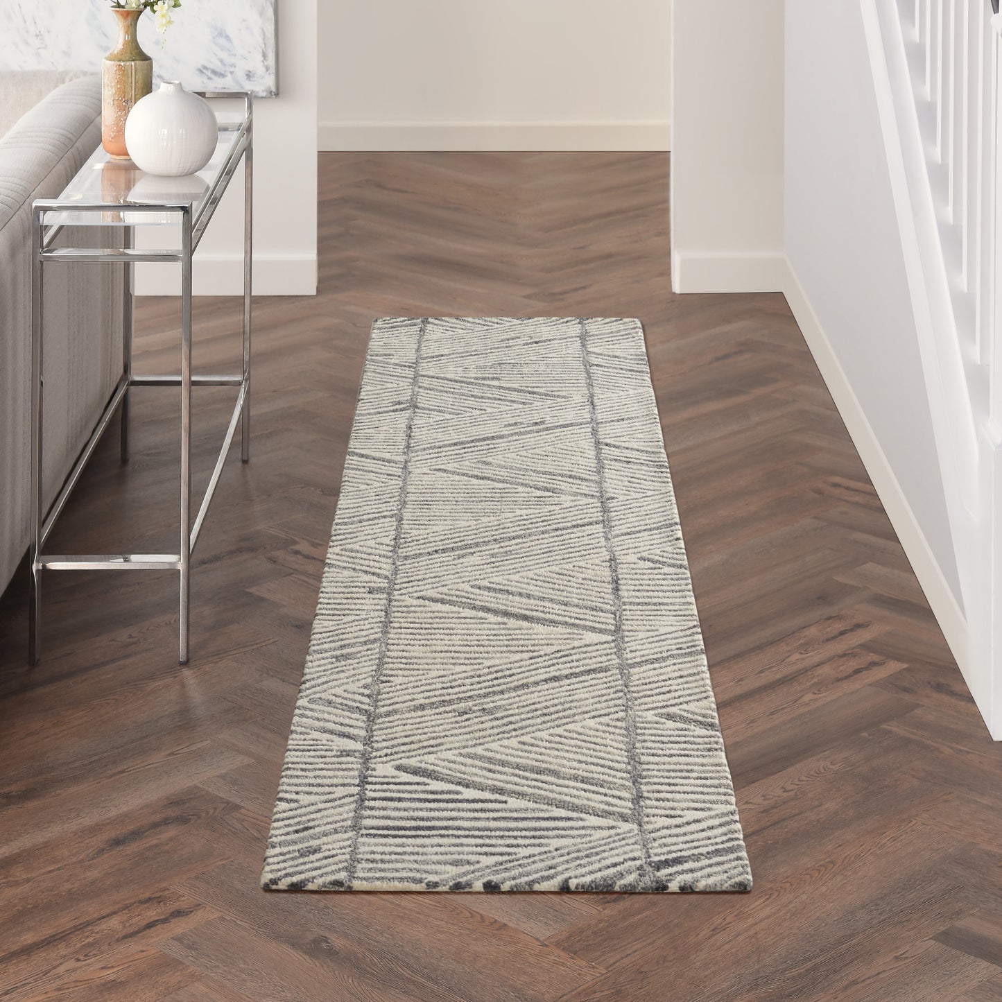Light gray geometric hallway runner rug with darker diagonal lines on a dark wood herringbone floor.
