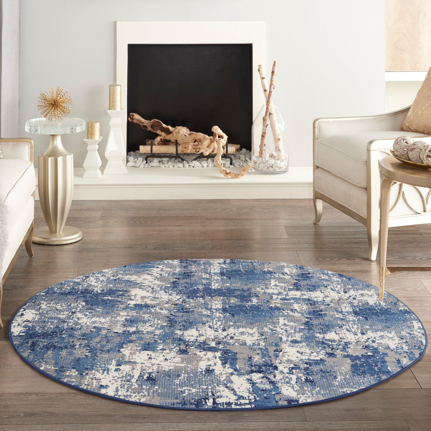 Round blue abstract rug on wood floor in a modern living room with white seating & a fireplace.