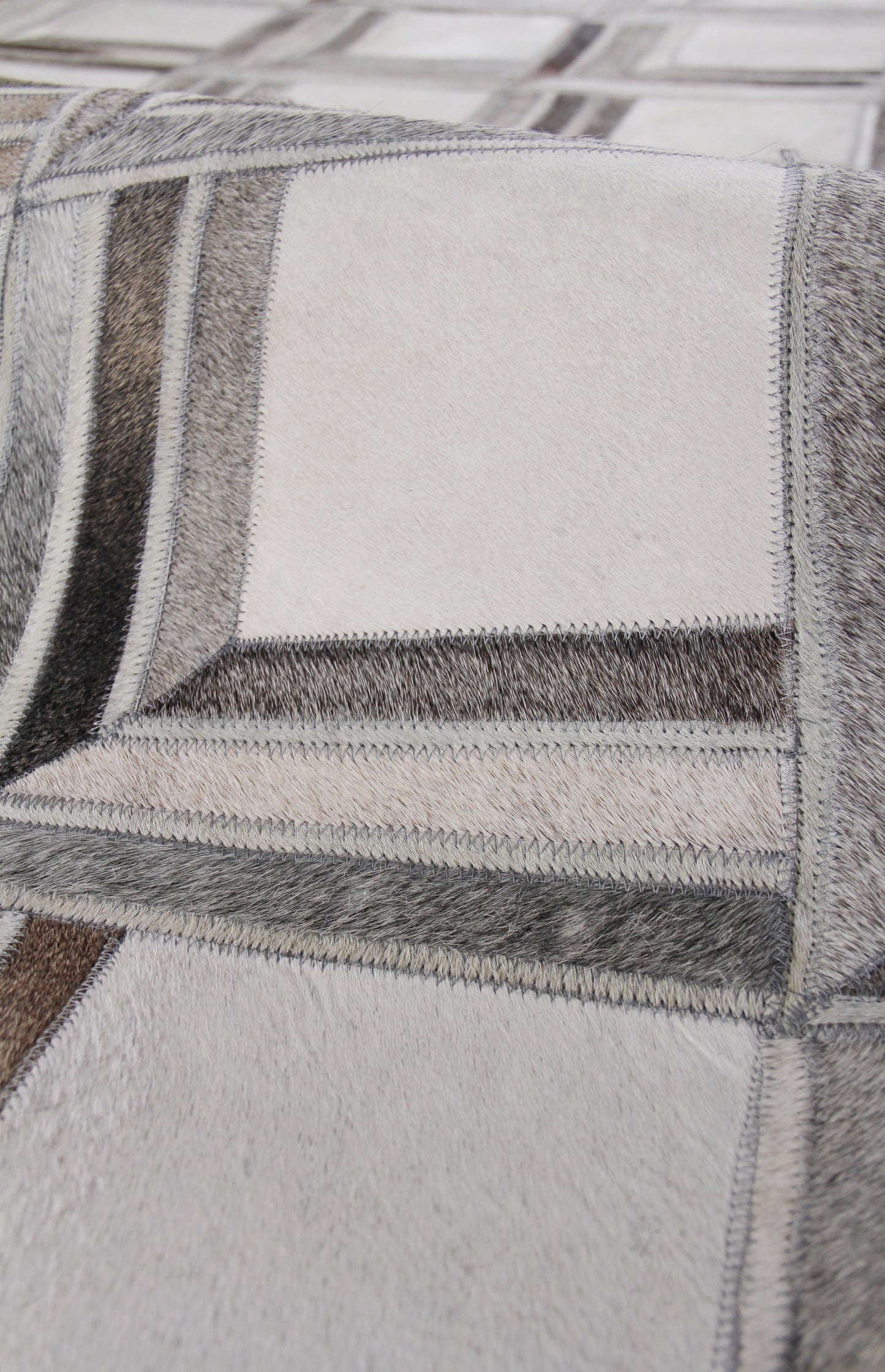 Close-up of patchwork natural hide rug, hand-stitched with zigzag seams in gray, beige, taupe tones.