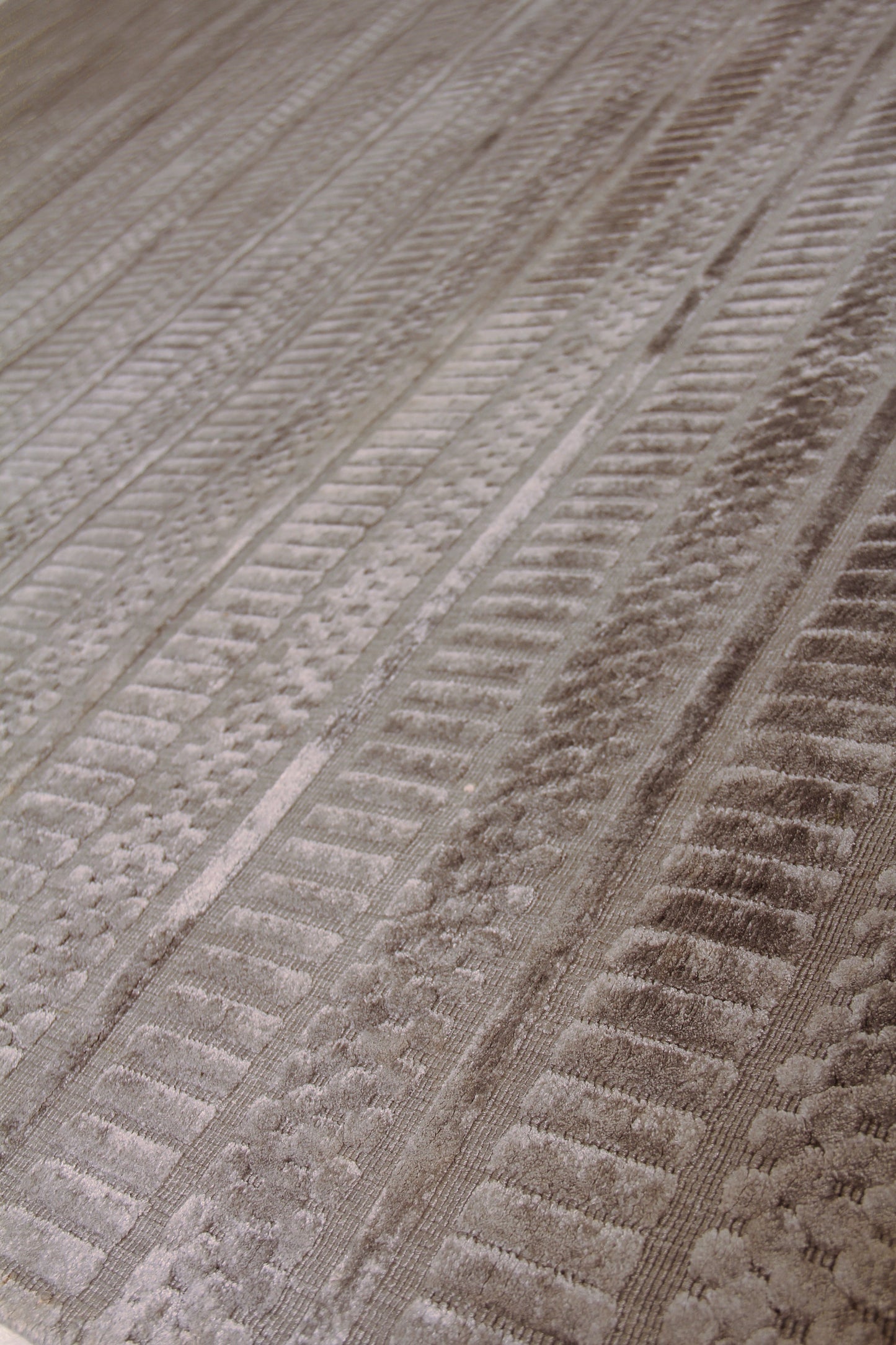 Taupe textured rug close-up featuring parallel ribbed stripes and a soft plush pile.