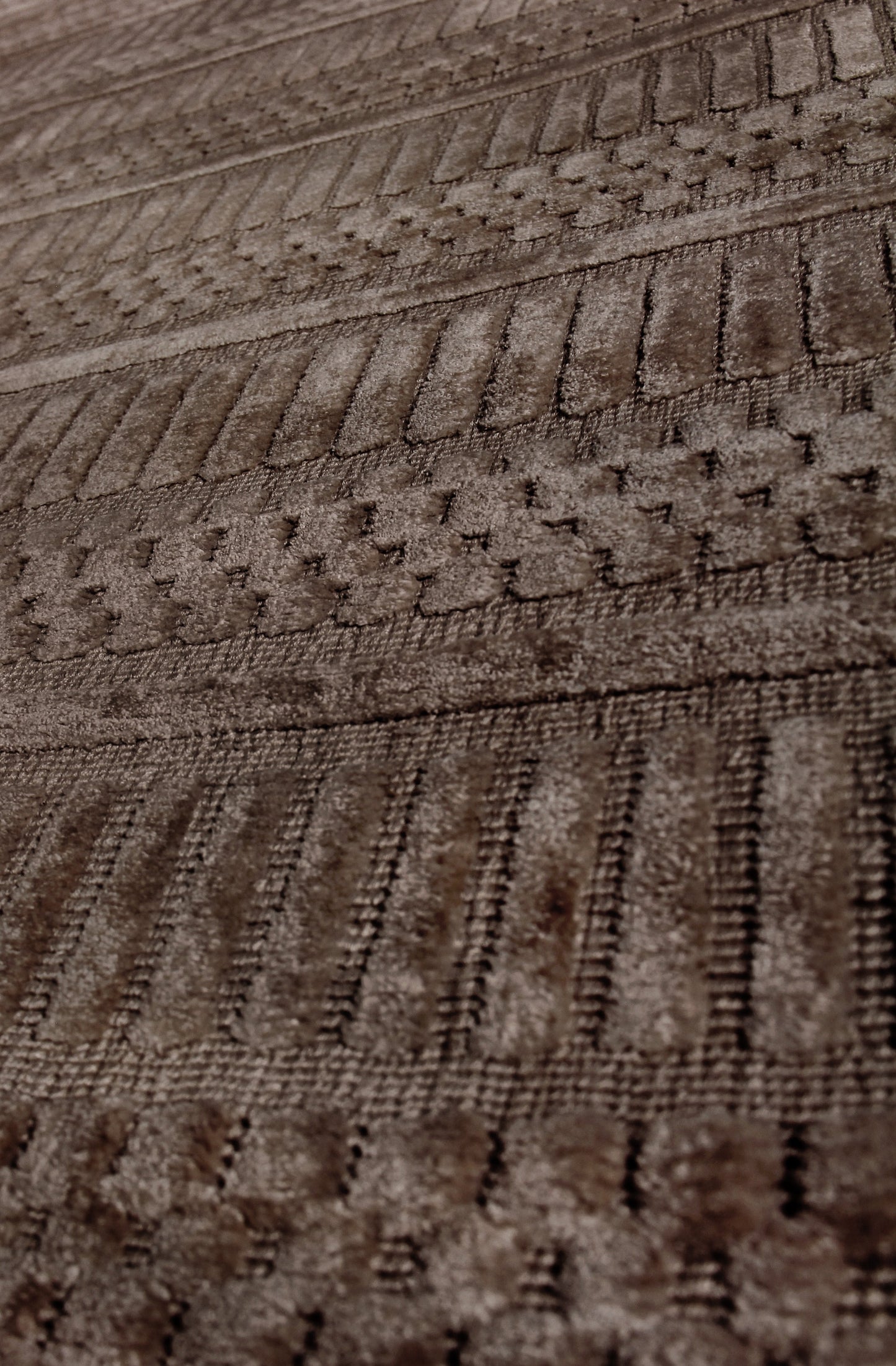 Brown textured rug with raised geometric patterns and ribbed stripes in warm tones.