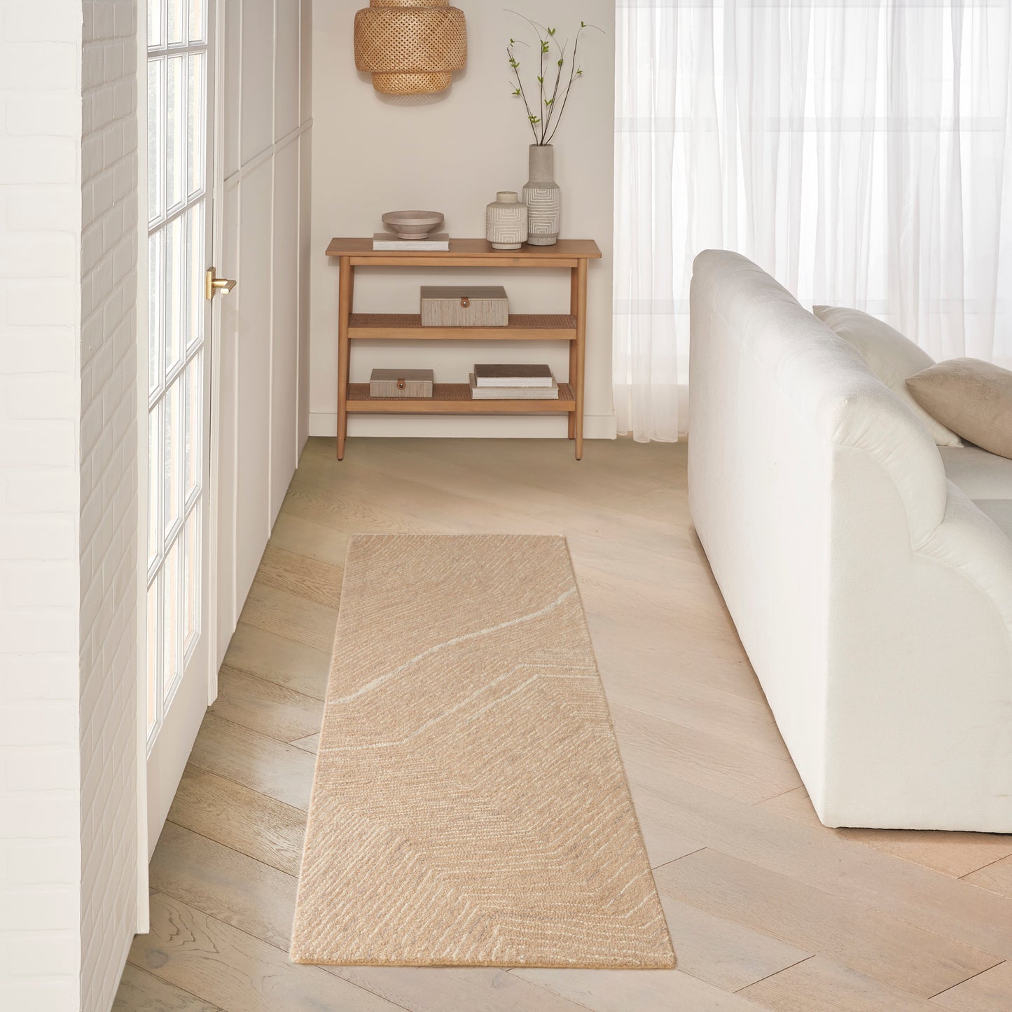 Neutral living room featuring a long beige woven runner rug, light wood console table, white sofa and sheer curtains.