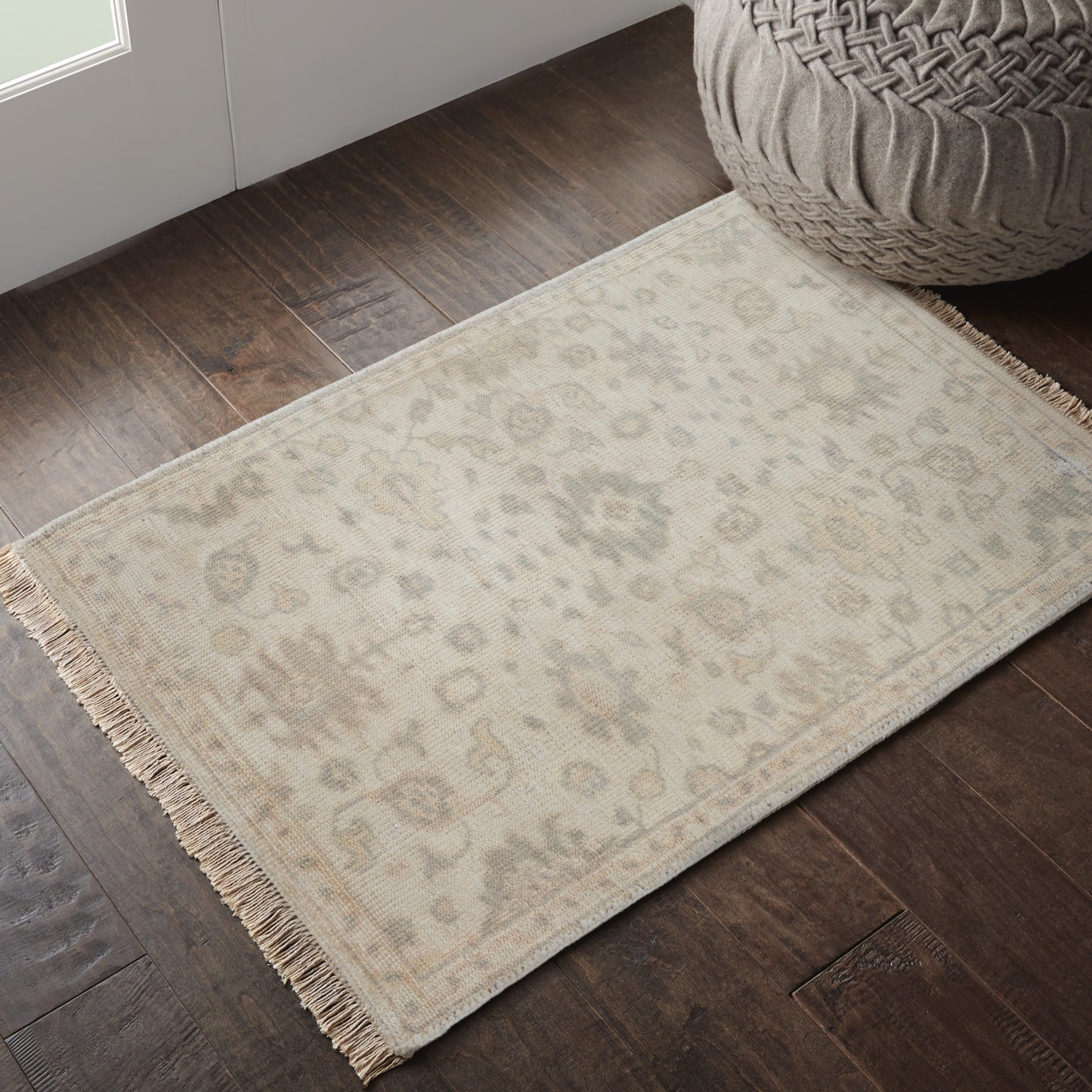 Soft beige blur dominates center; bottom reveals dark wood floor with a beige fringed rug.