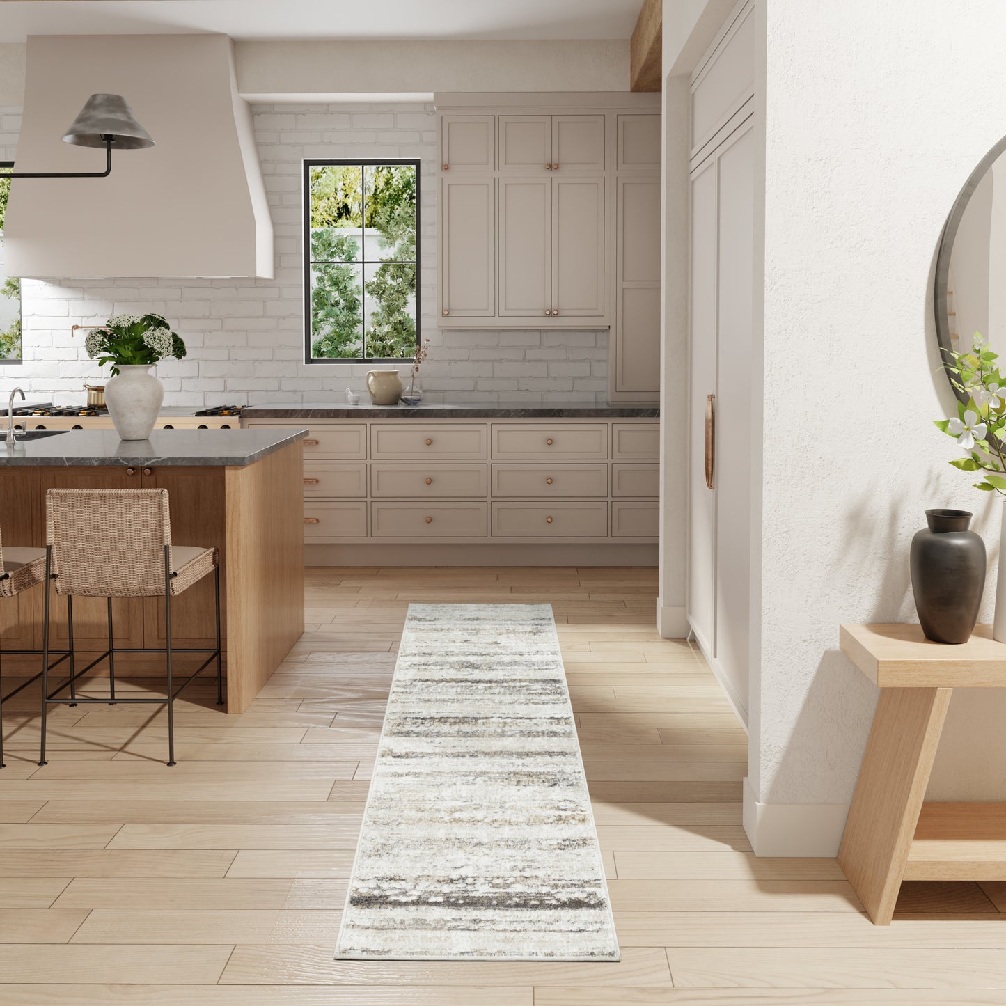 Bright white kitchen with light wood floors, island and stools, cabinets, subway tile, and a distressed gray rug runner.
