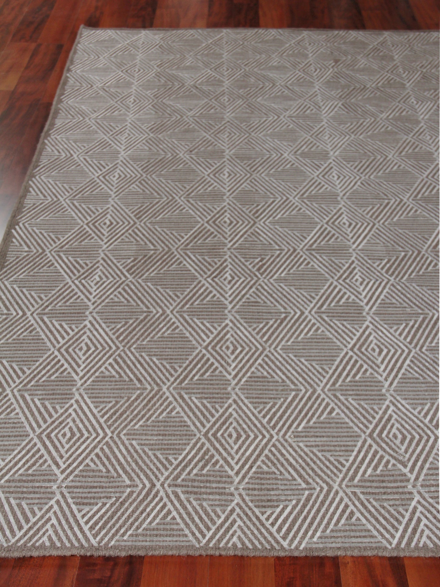 Grey geometric woven area rug with diamond and triangle pattern on dark hardwood floor