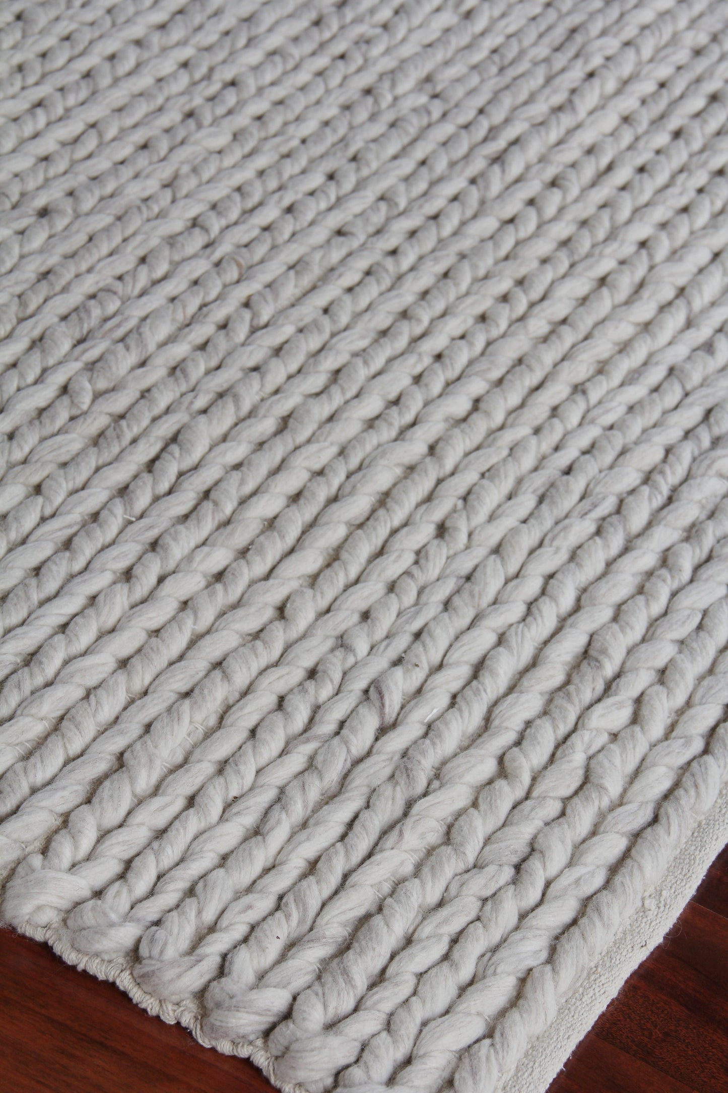 Cream chunky knit wool rug with thick rope-like loops and bound edge on dark hardwood floor