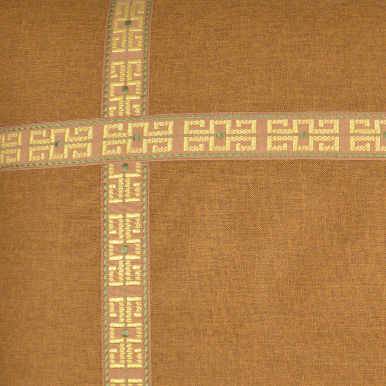 Pillow cover in burnt-orange fabric with beige Greek-key cross bands & mint green/pink accents; visible woven texture.