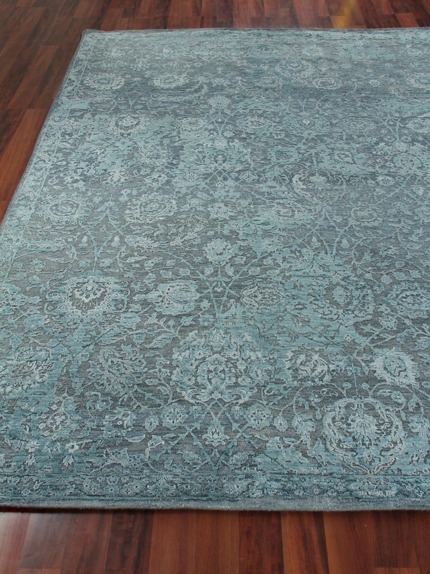 Teal blue rug with elaborate floral damask pattern on hardwood floor.