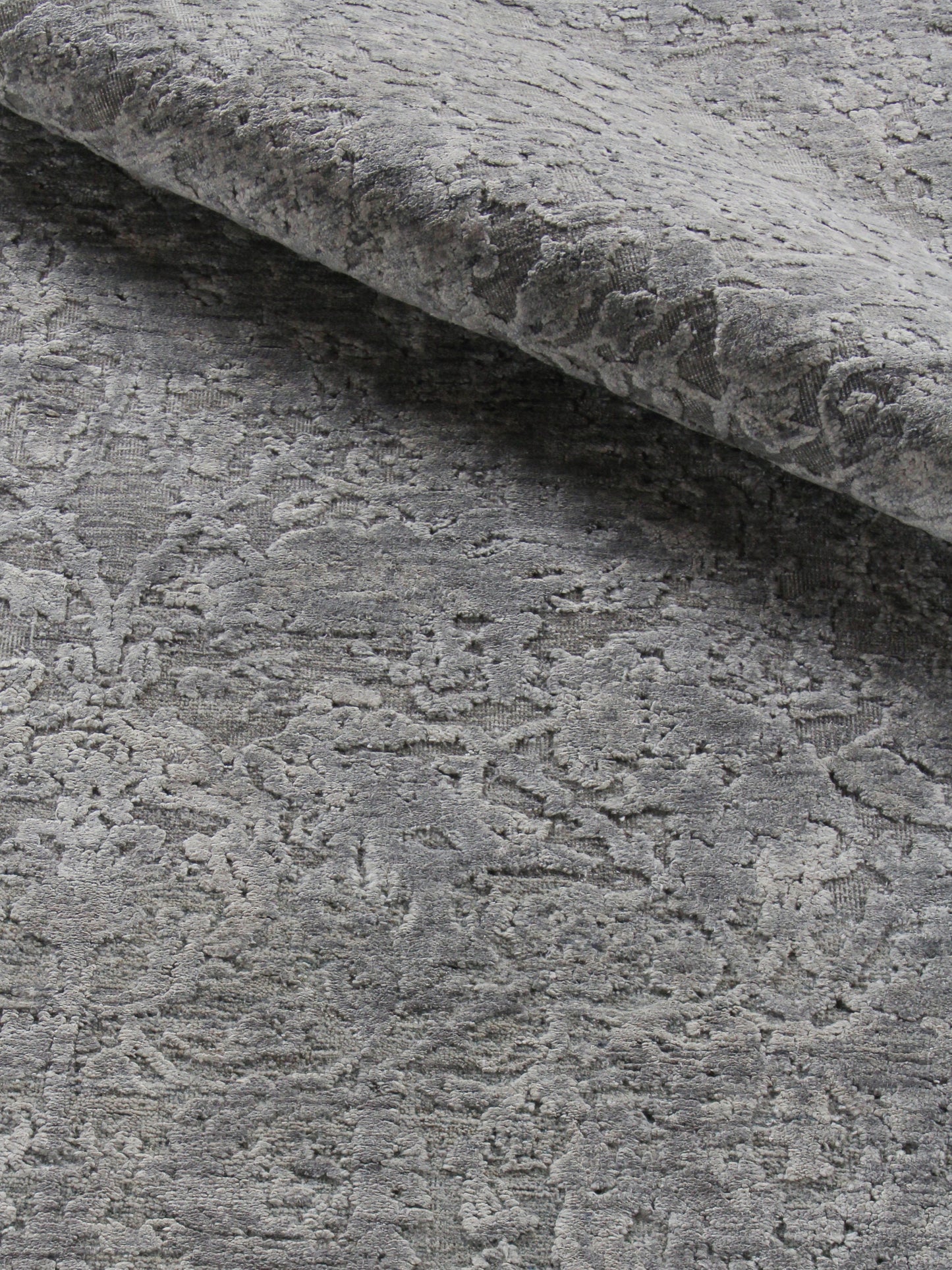 Gray damask velvet rug with raised floral pattern, folded to showcase its soft, plush texture.