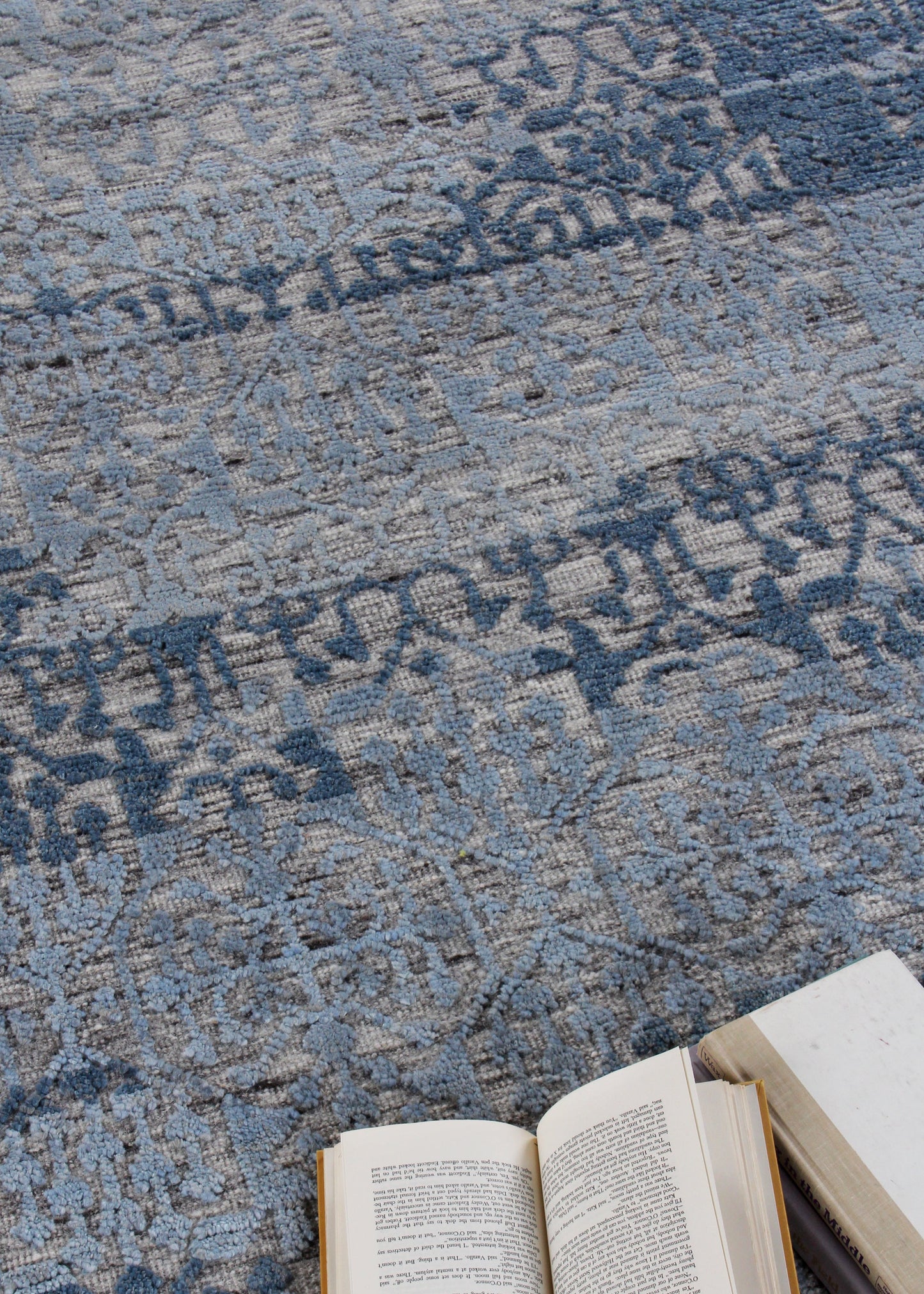 Blue patterned woven rug with a textured surface; open book and a closed book resting on it.