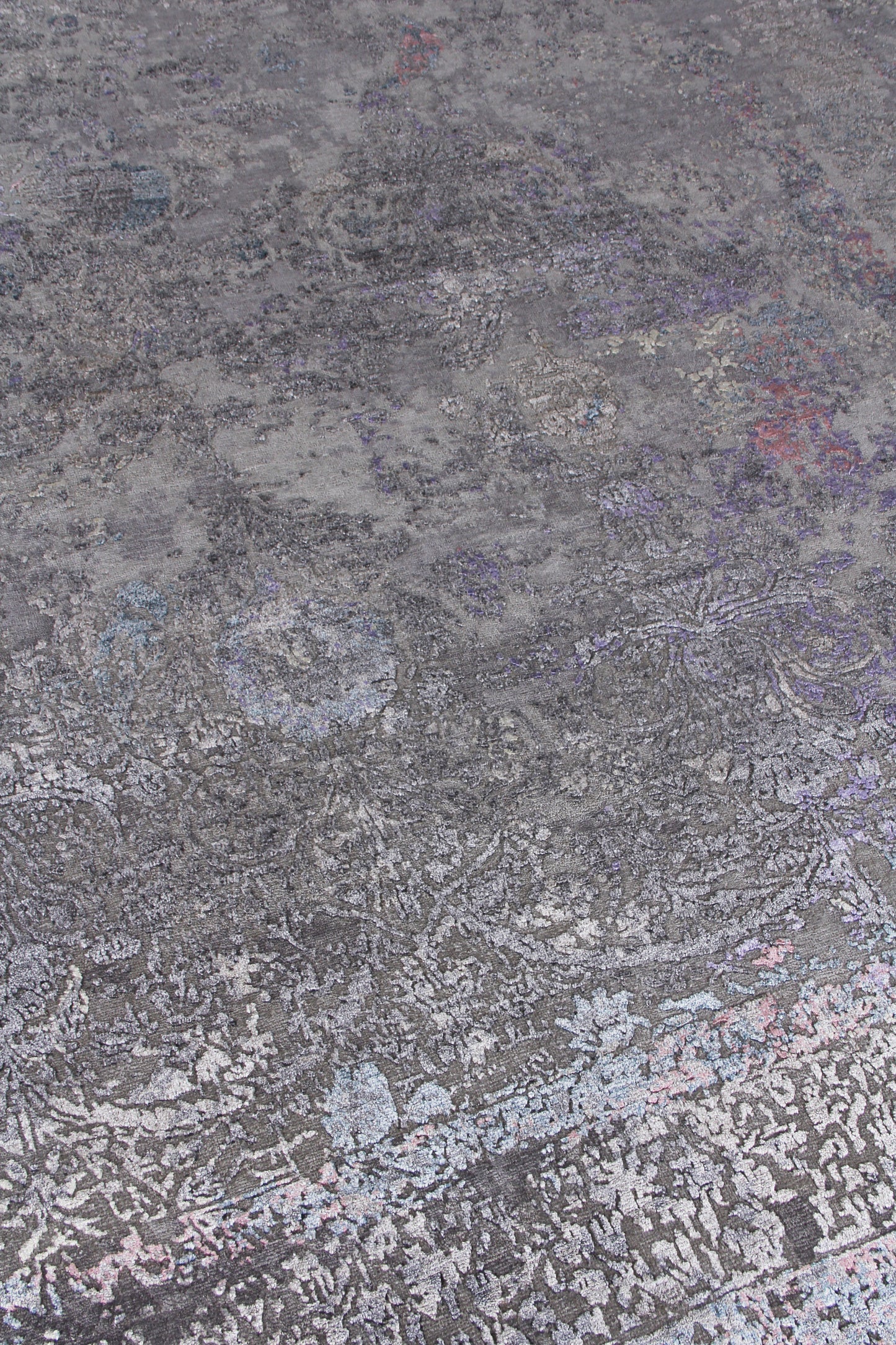 Rectangular gray distressed floral rug with muted lilac, blue and pink accents; vintage-style, soft woven texture.