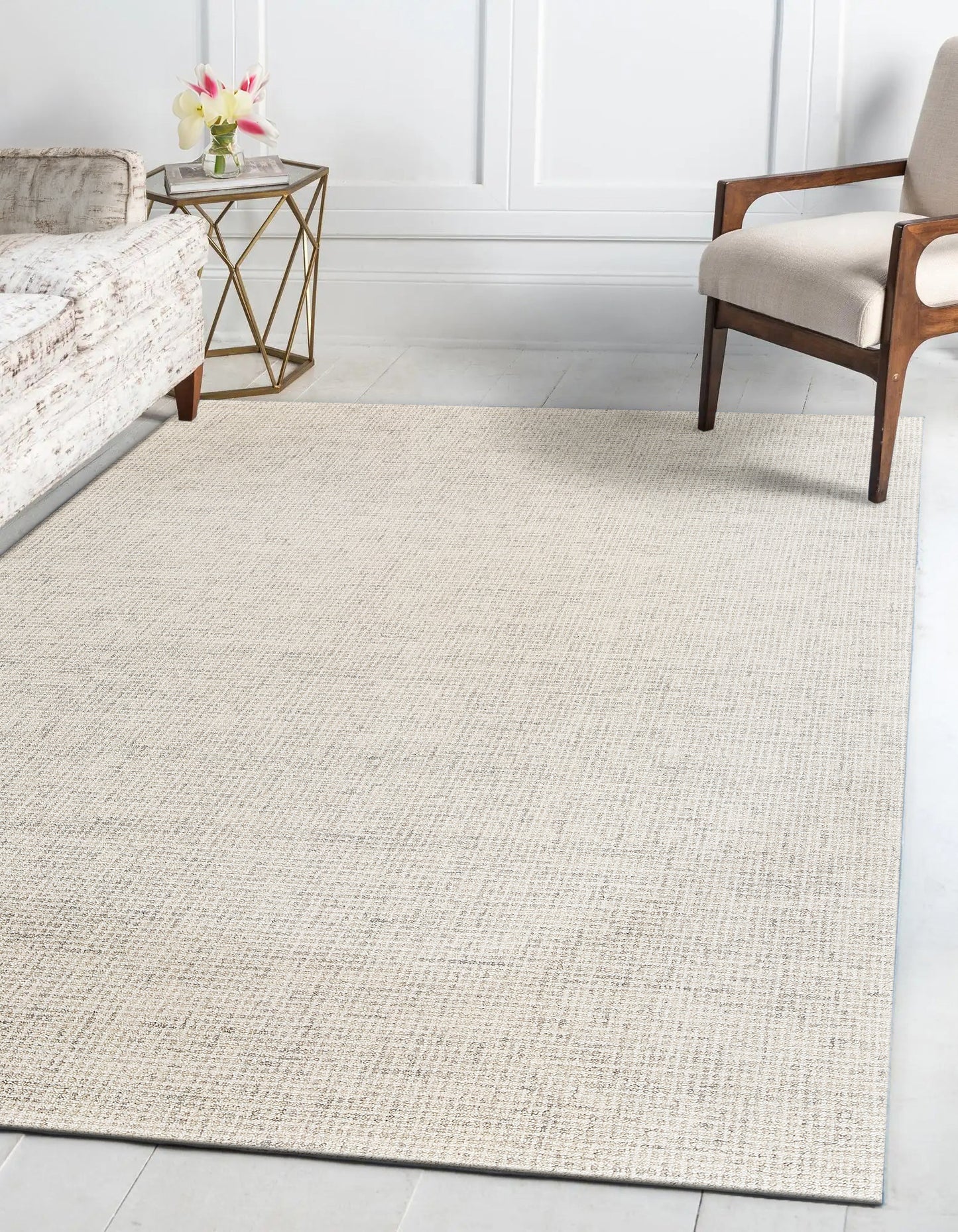 Beige textured area rug in a bright living room with a wooden-armchair, a glass-top gold geometric side table, and pink flowers.
