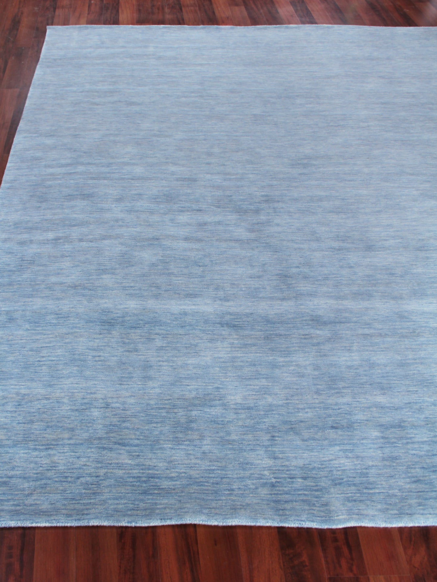 Rectangular light blue textured area rug resting on dark hardwood floor.