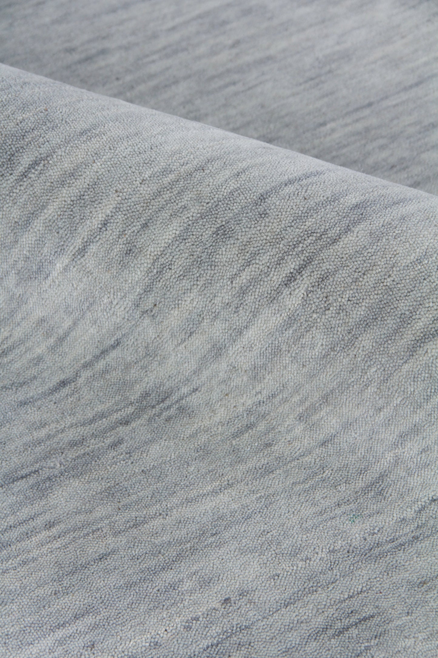 Close-up of soft gray-blue heather rug with subtle marled texture and folded edge.
