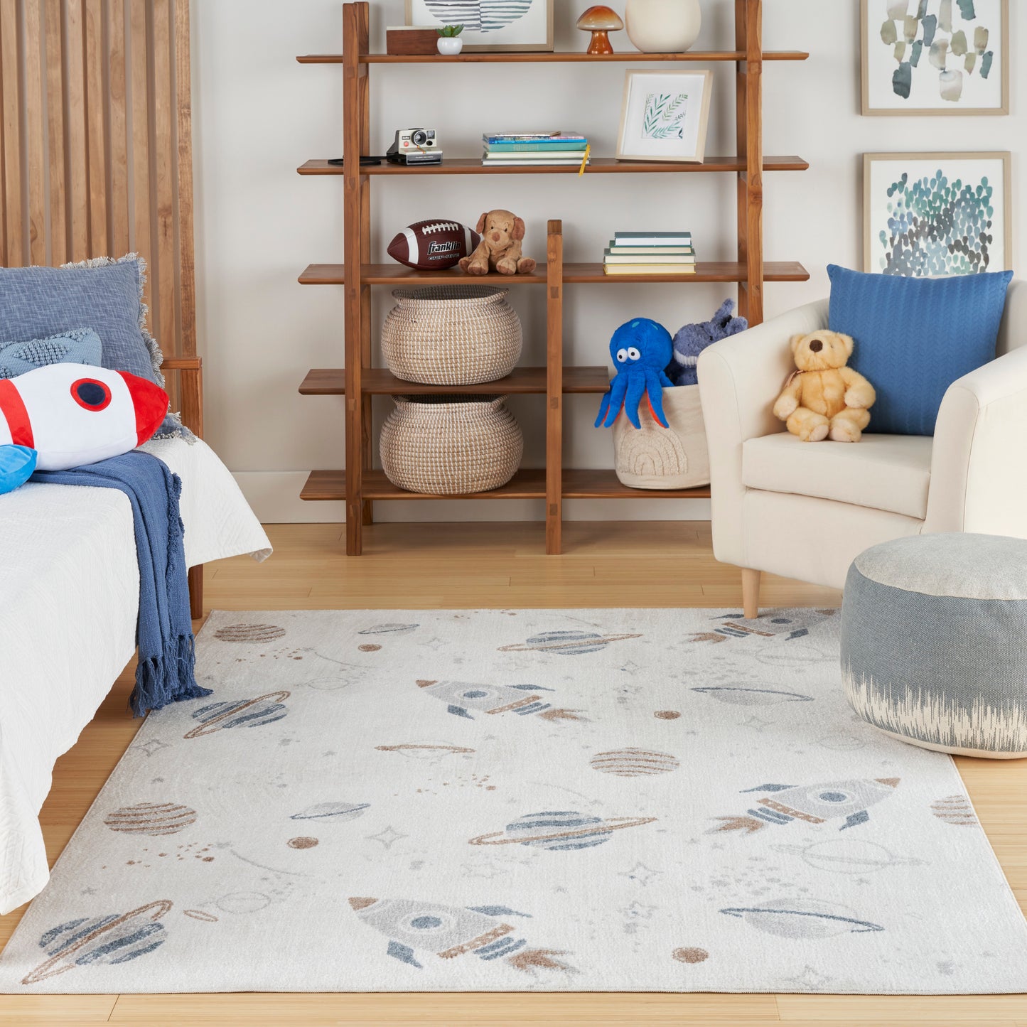 Light kid's rug with rockets and planets in blue/beige tones, in a cozy room with wooden bookshelf and stuffed toys.