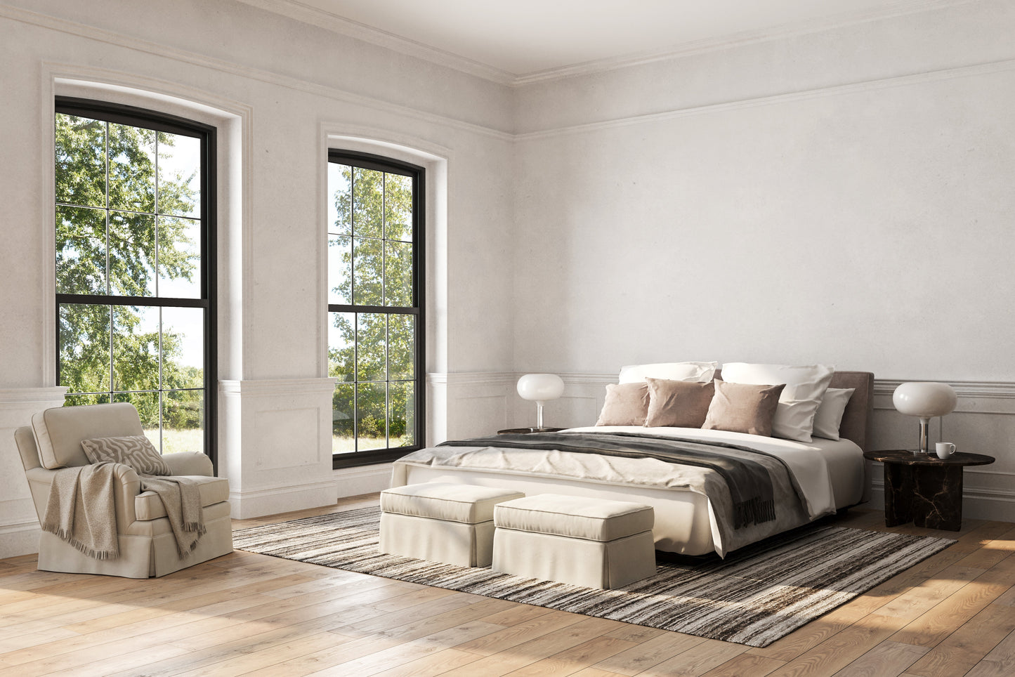 Bright modern bedroom with king bed in cream bedding, ottoman at foot, striped rug, two round lamps, and an armchair by large windows.