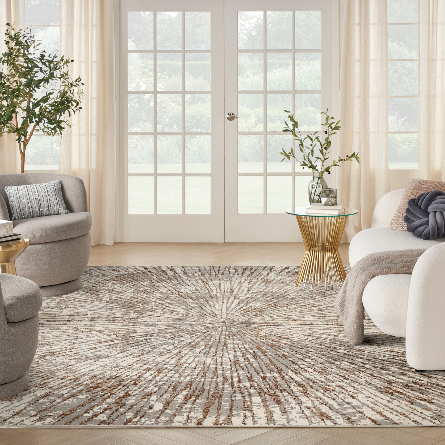 Bright neutral living room with glass doors, a sunburst beige rug, round gray chairs, and gold-toned side tables.