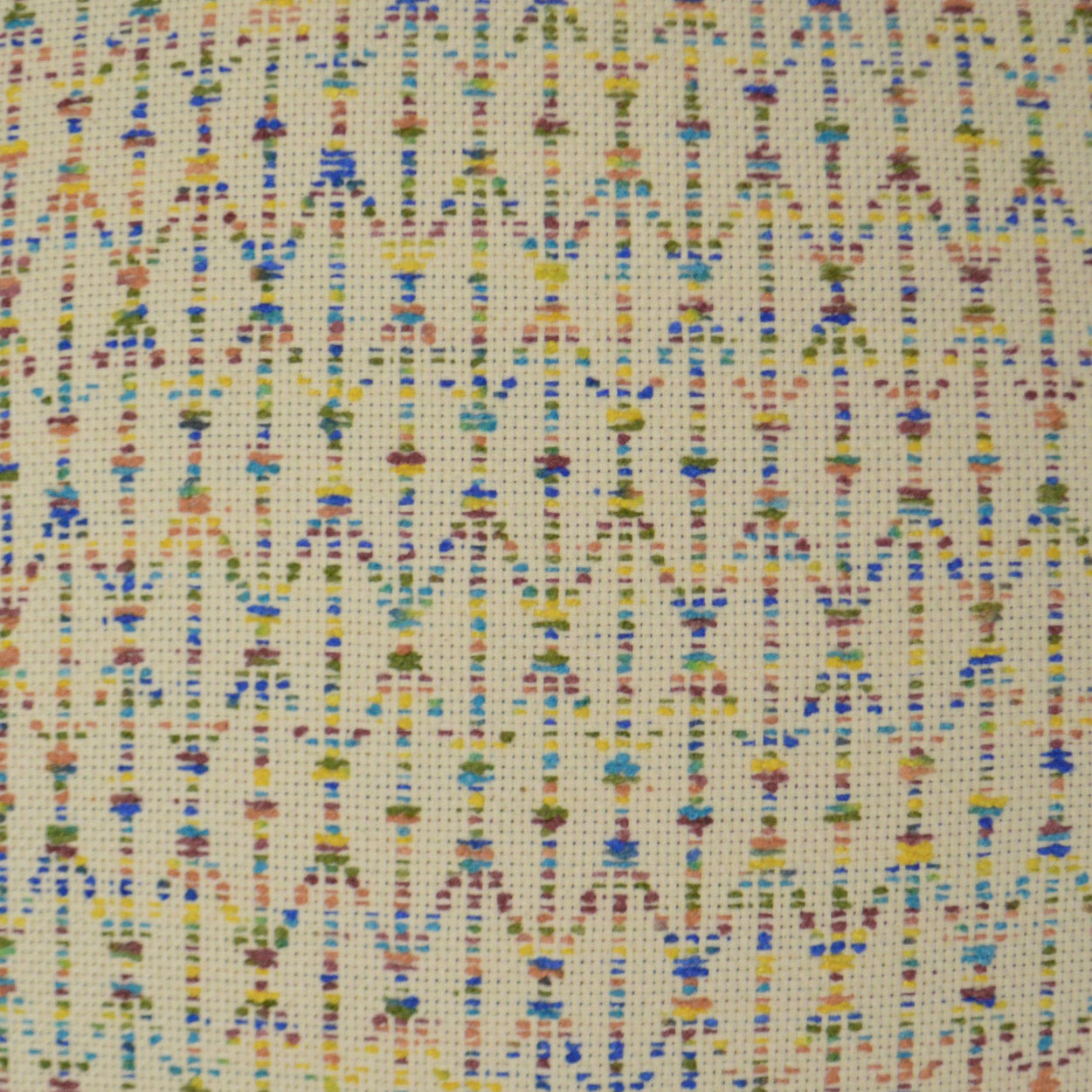 Cream woven fabric with tiny multicolor geometric motifs in vertical rows; lightweight textile for sewing or crafts.