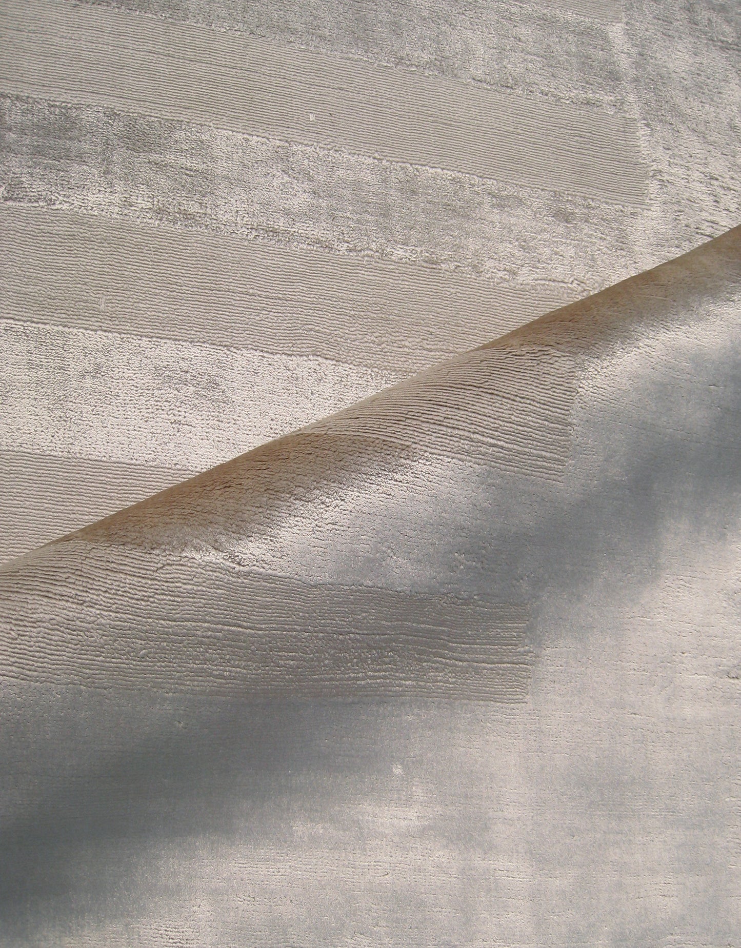 Curl of metallic beige rug with brushed horizontal stripes against a light gray textured surface.