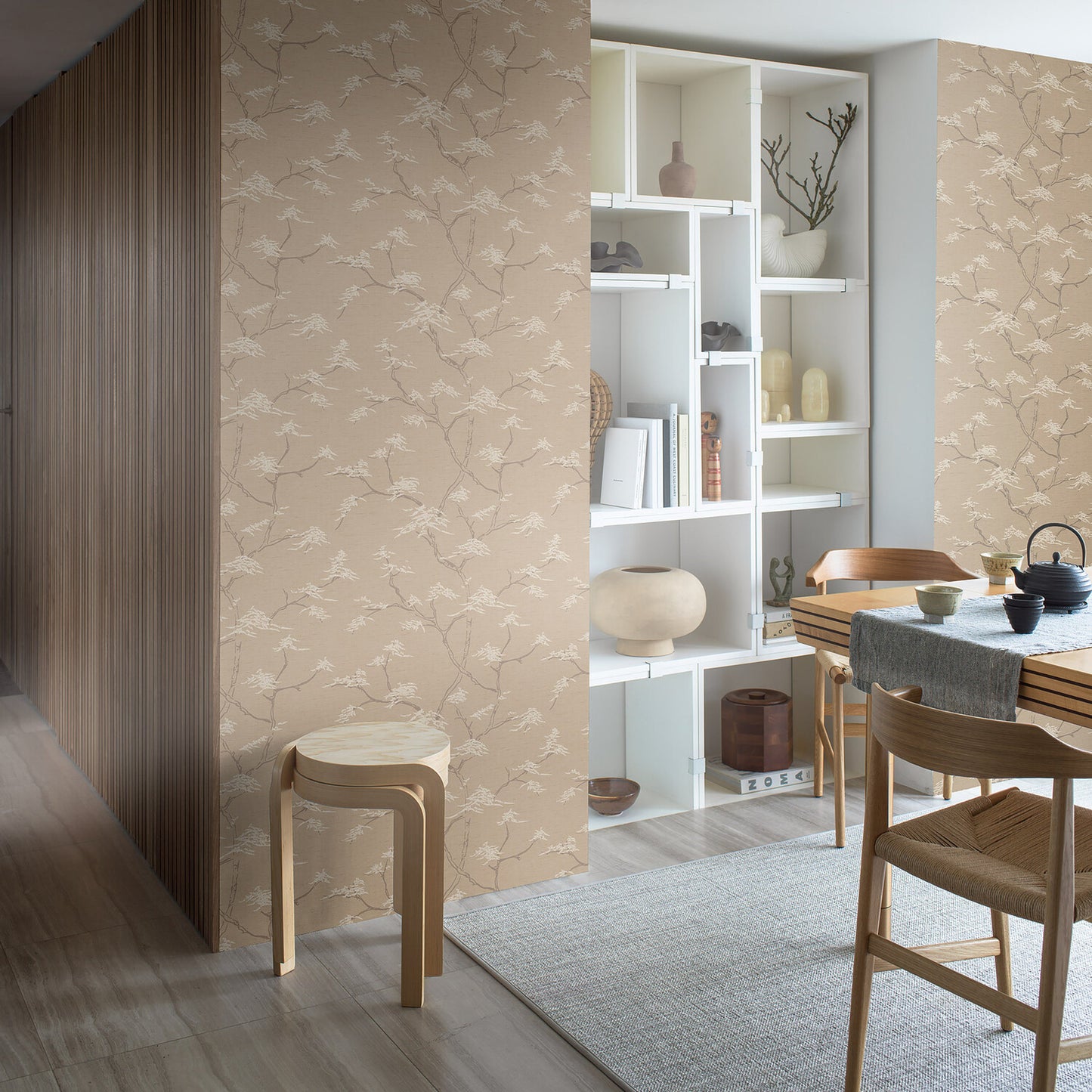 Beige floral wallpaper on wall beside white modular shelves, light wood dining table with chairs, gray rug.