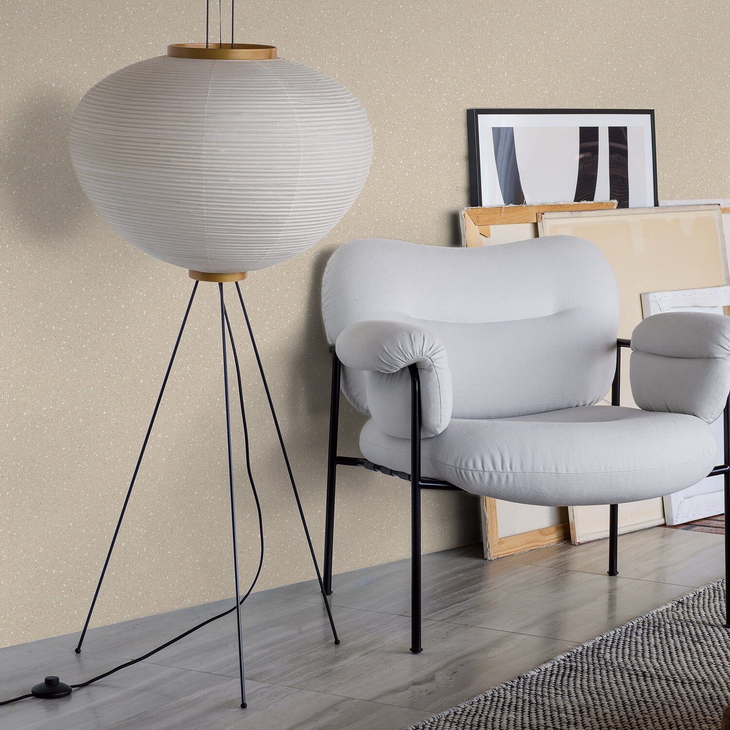 White round paper lantern pendant on tripod stand beside a light gray curved-arm lounge chair in a modern living room.