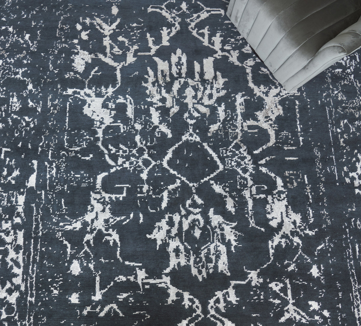 Navy distressed oriental rug with ivory floral medallion motif; plush dark pile, corner of gray tufted sofa visible.