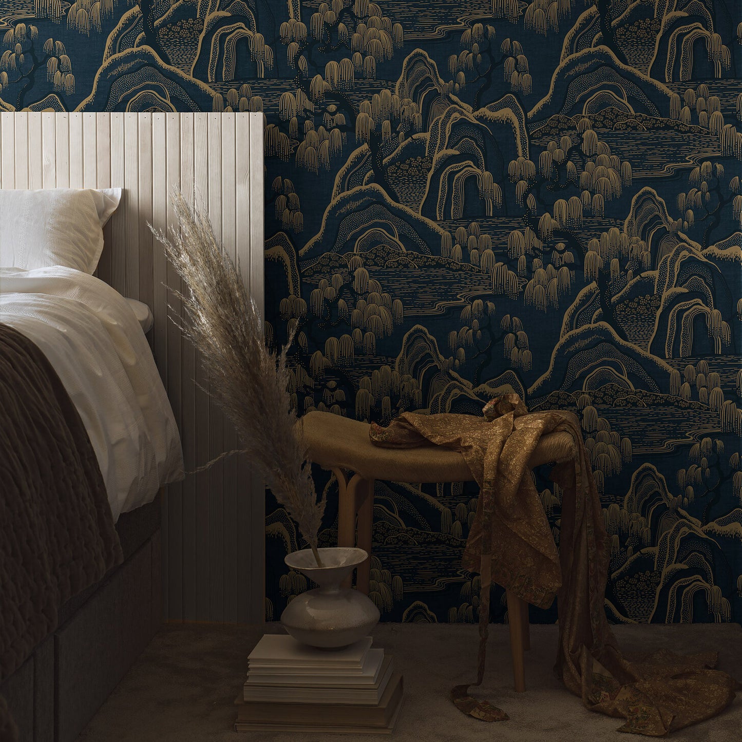 Borastapeter Indigo Garden 3132 wallpaper featuring a stylized oriental garden in indigo and gold, with willow trees and scenic hills. Displayed on a feature wall, ideal for elegant interior design in bedrooms or living spaces.