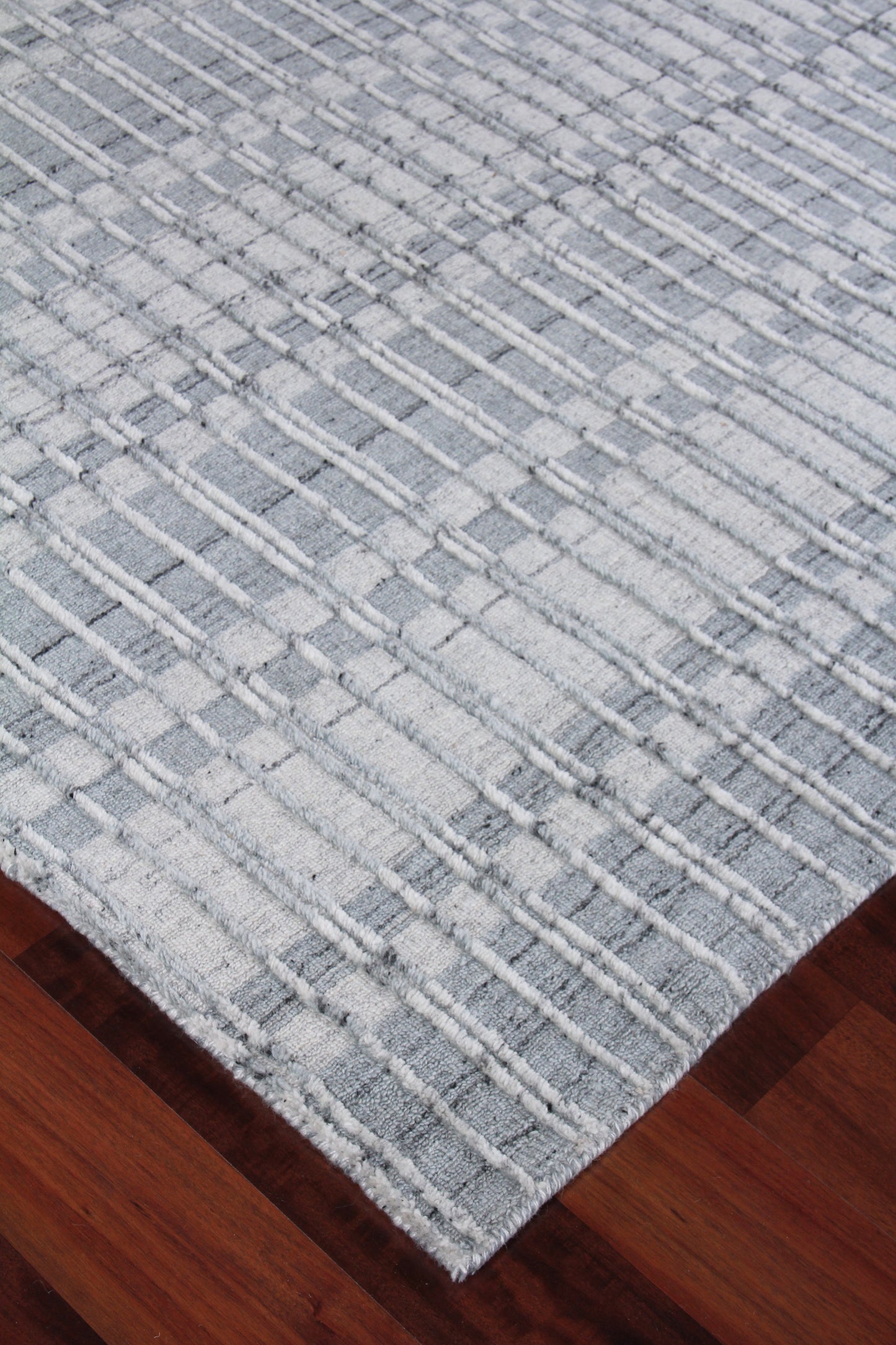 Light gray woven rug with a white raised grid pattern, rectangular shape on dark wood flooring.