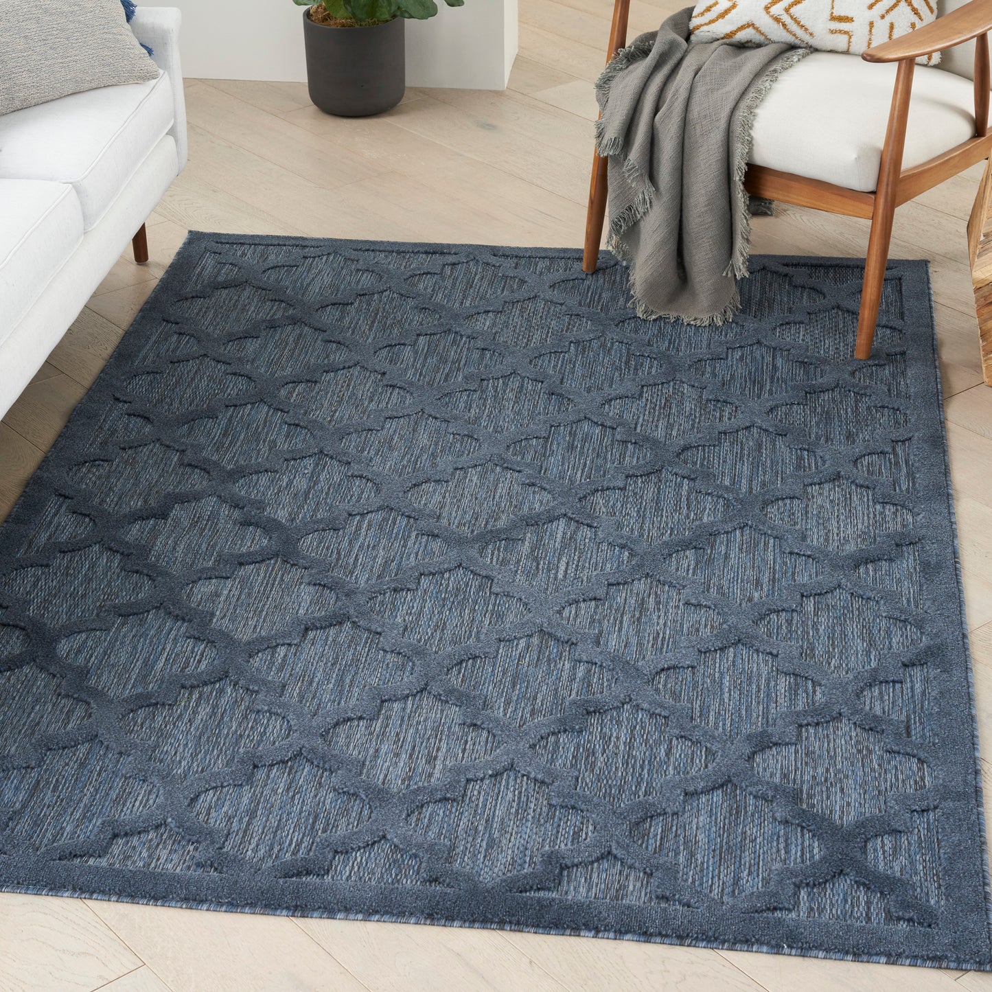 Dark blue woven area rug with repeating geometric lattice pattern on light wood floor in a cozy living room.