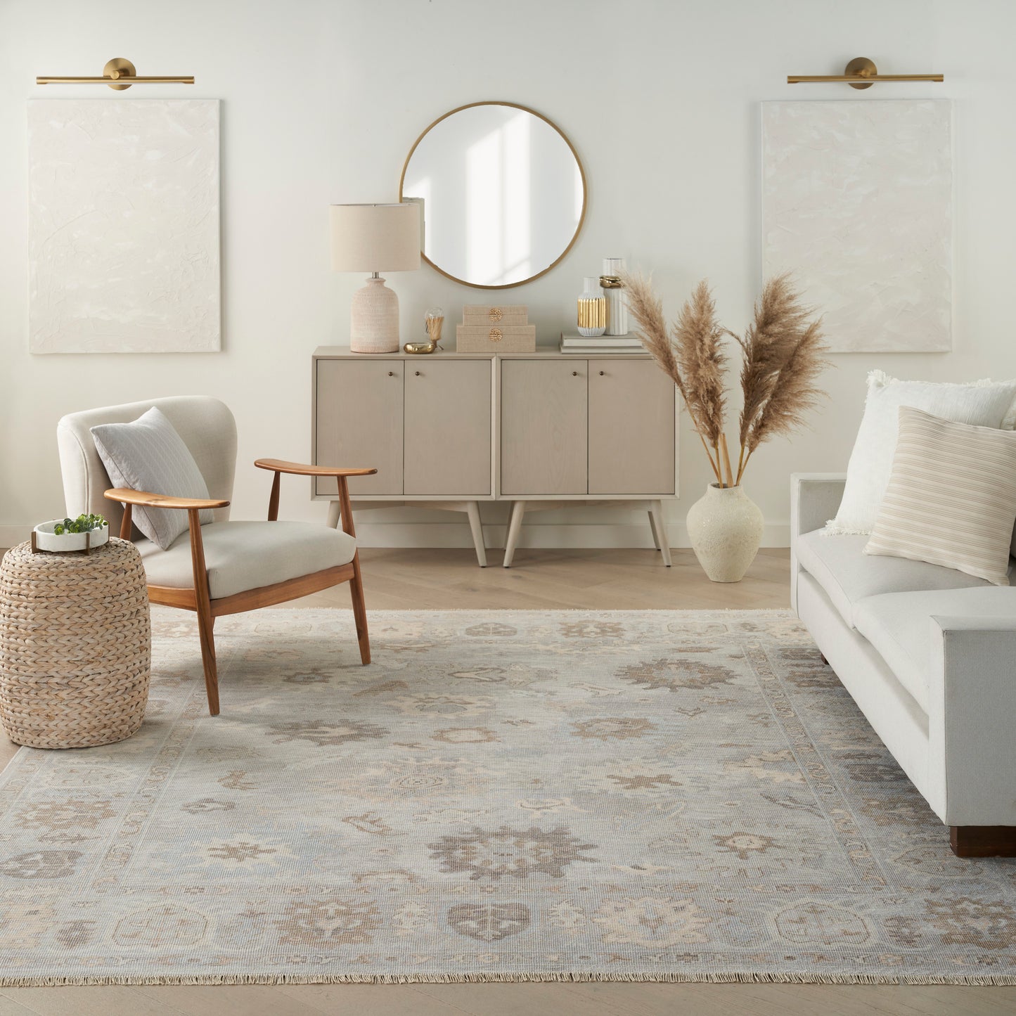 Neutral living room with light sofa, wooden armchair, round mirror, beige sideboard, pampas grass vase, patterned rug.
