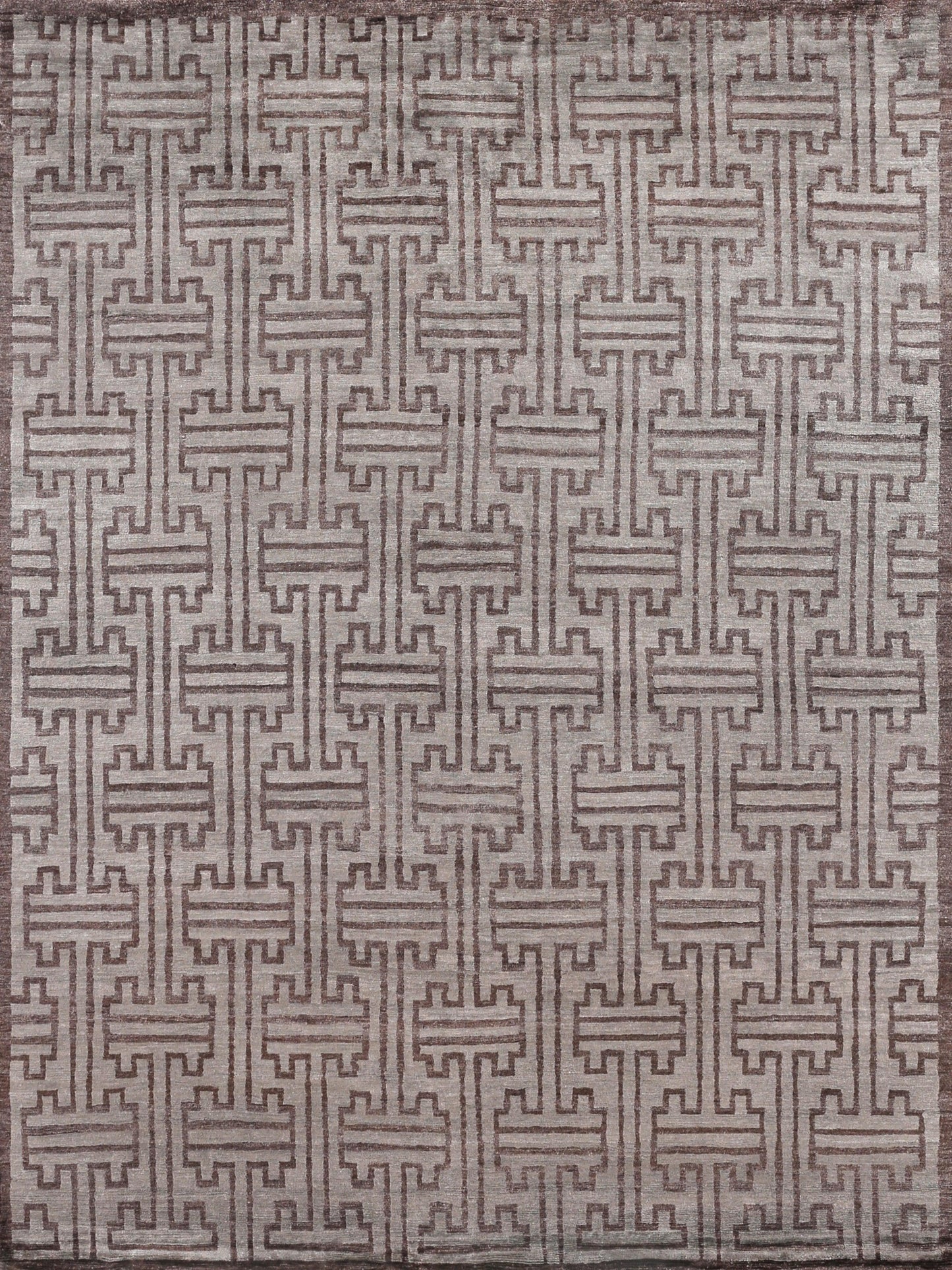 Rectangular area rug featuring an intricate geometric pattern in muted earthy tones of brown and gray, soft texture.