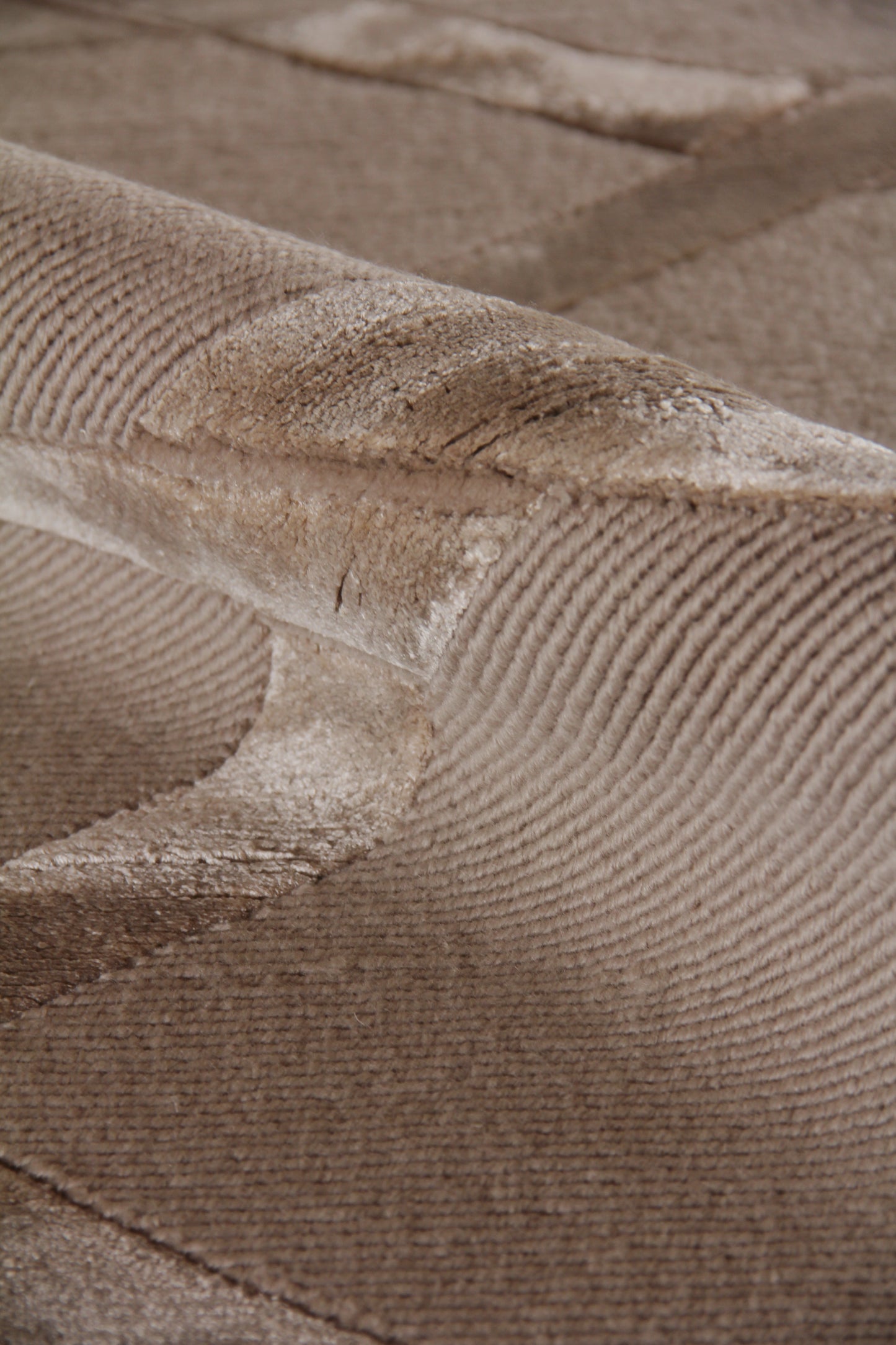 Tan velvet-look indoor hand-knotted rug, 4' x 6', with a curved stitched seam and soft folded edge.