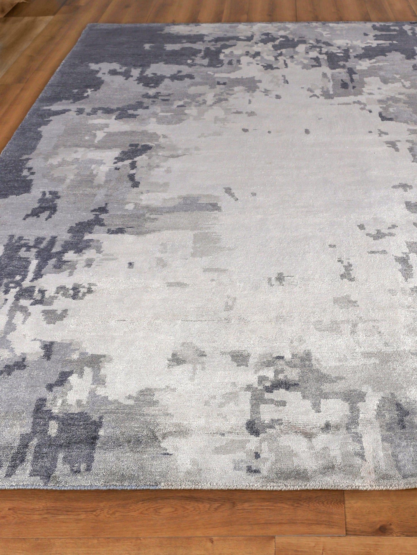 Abstract grey area rug with silver and blue-gray tones, rectangular, modern decor, on wooden floor.