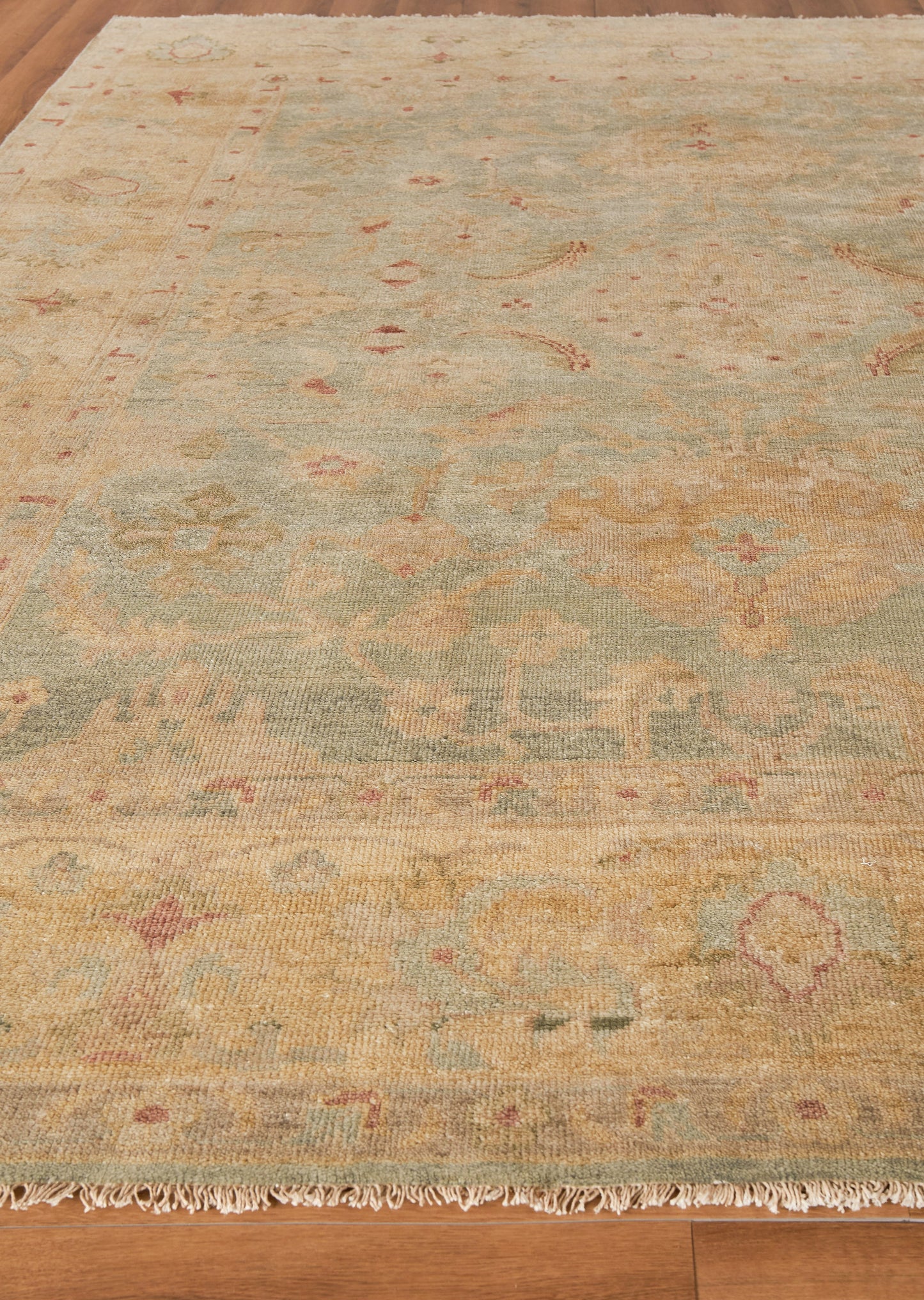 Pastel oriental rug, rectangular with sage green, ochre, peach and pink floral motifs; fringed edges on floor.