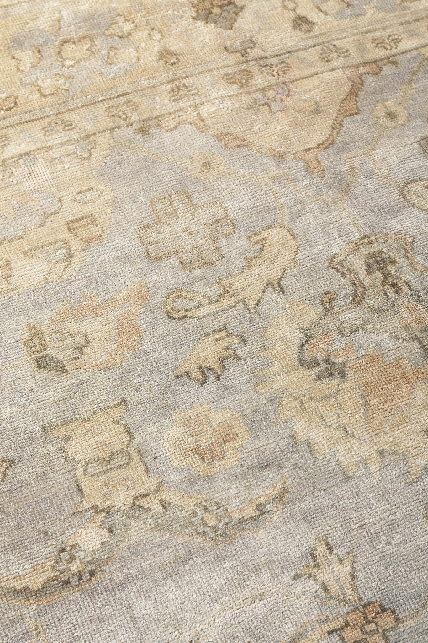 Distressed oriental rug in beige, pale blue-gray and taupe with faded floral motifs.