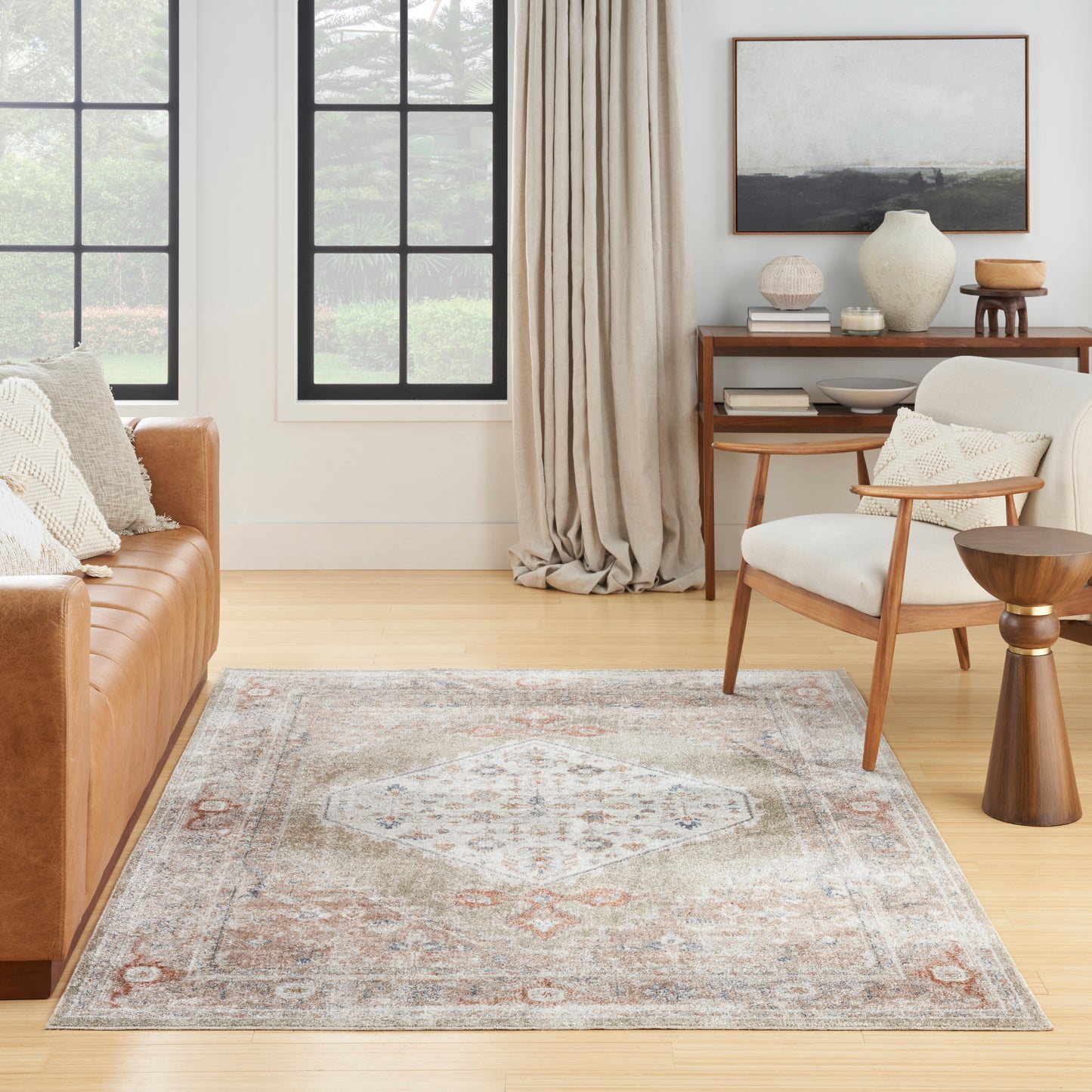 Cozy living room with a muted geometric rug, tan leather sofa, mid-century chair, wooden side table, beige curtains.