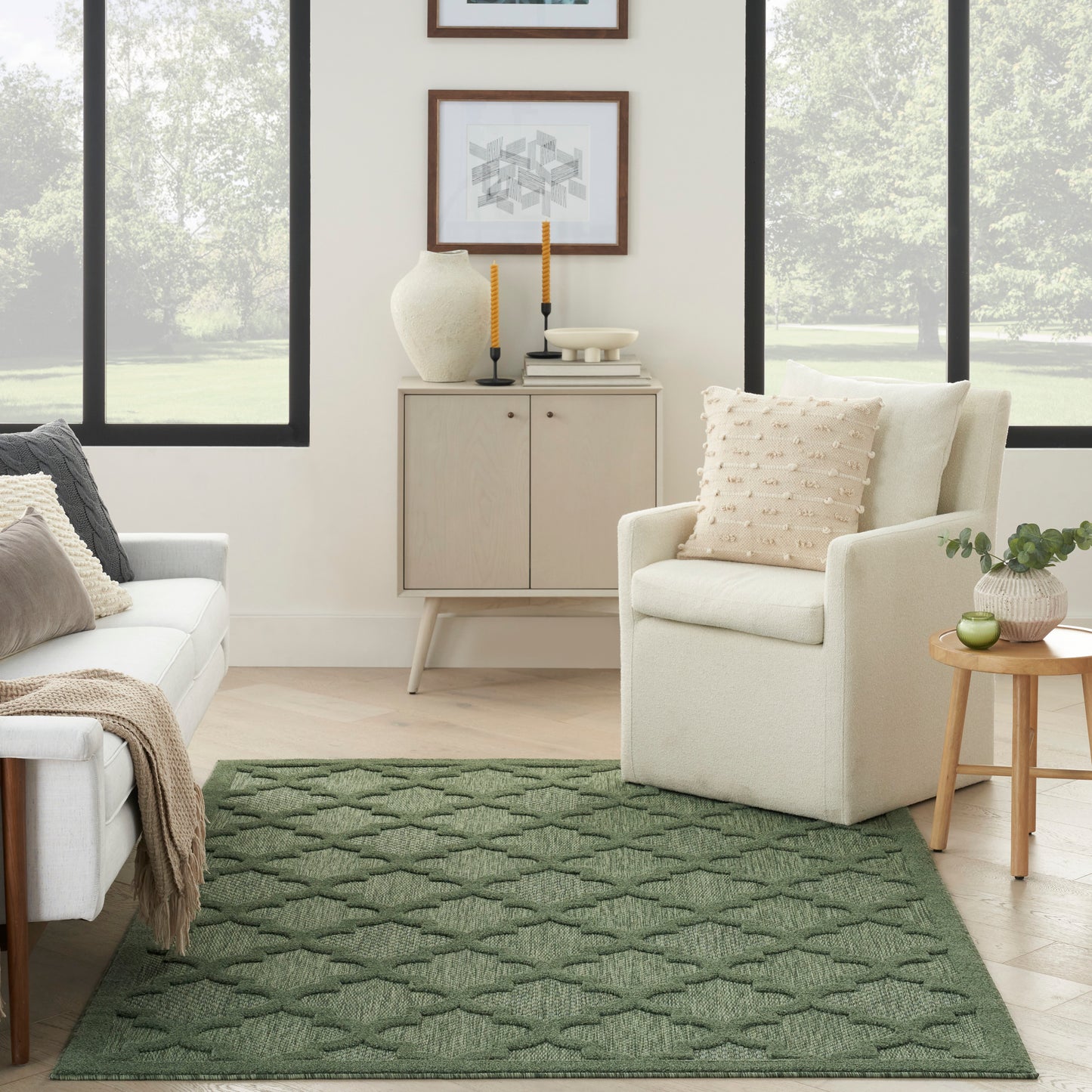 Green textured geometric area rug in a bright living room with cream sofa, beige armchair, light wood cabinet, and plant.