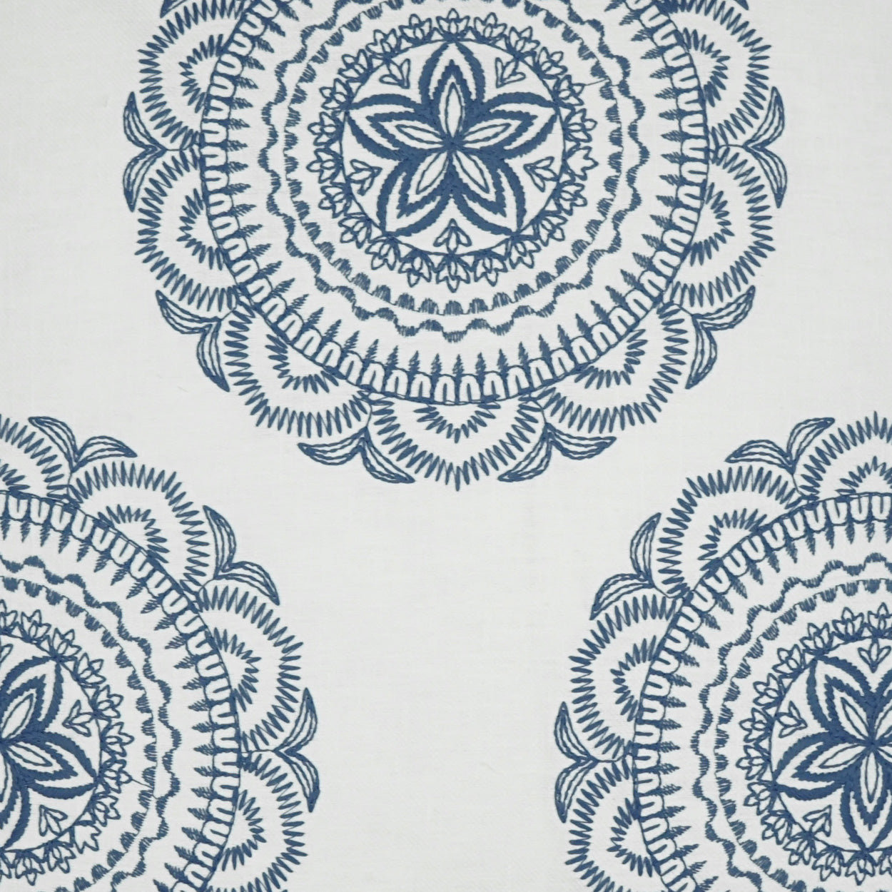 Blue mandala-style circular motifs on white fabric, featuring intricate concentric patterns.