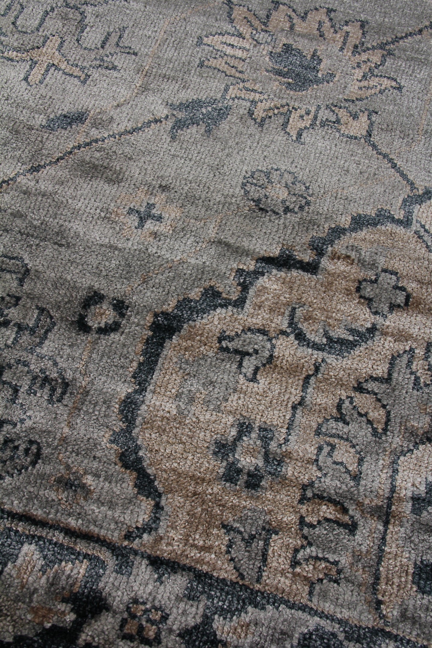 Close-up of a bamboo hand-knotted rug in beige-gray tones with blue-gray floral medallions and an ornate border.