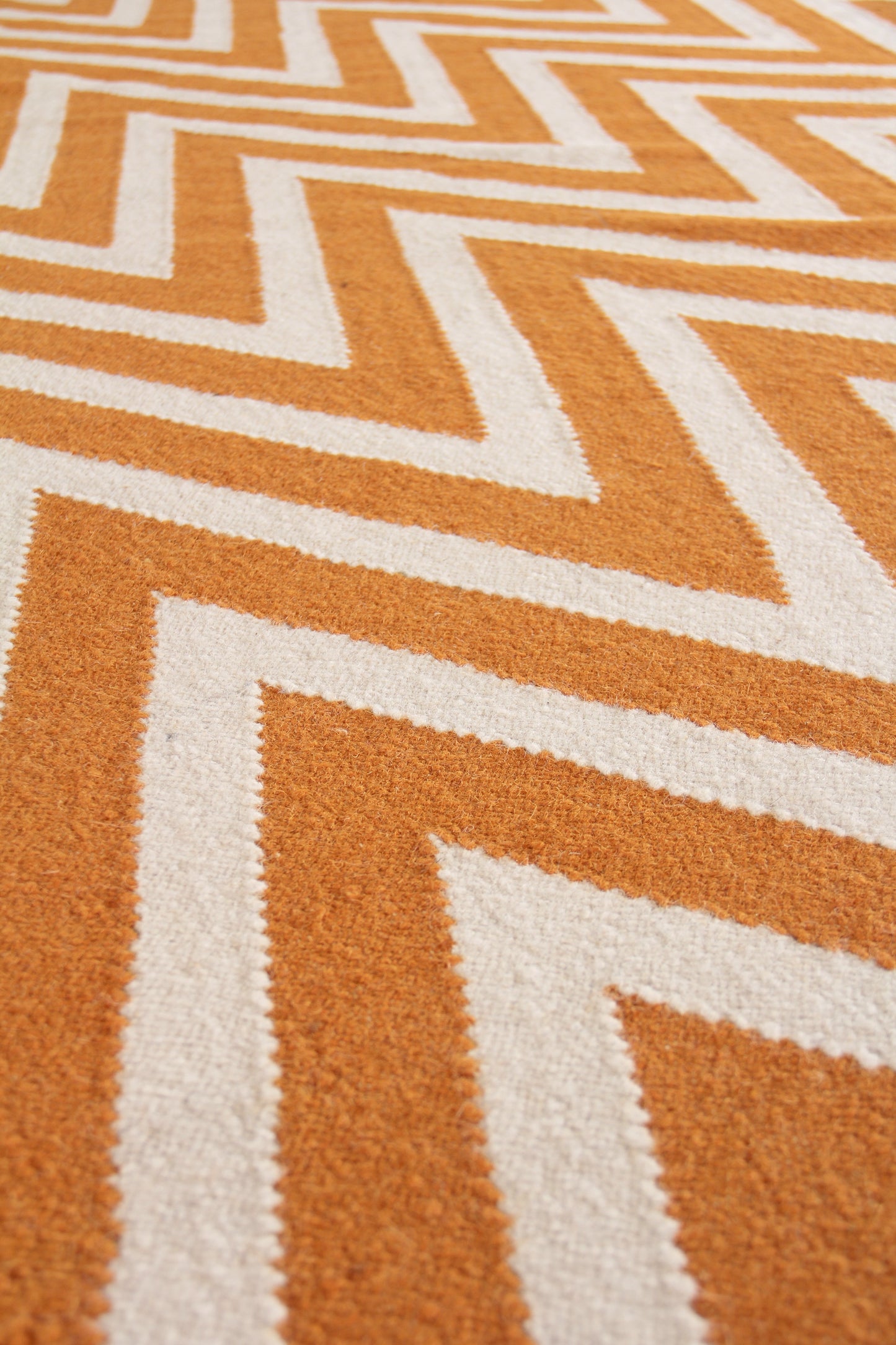 Close-up of orange and white geometric chevron flatweave indoor rug.